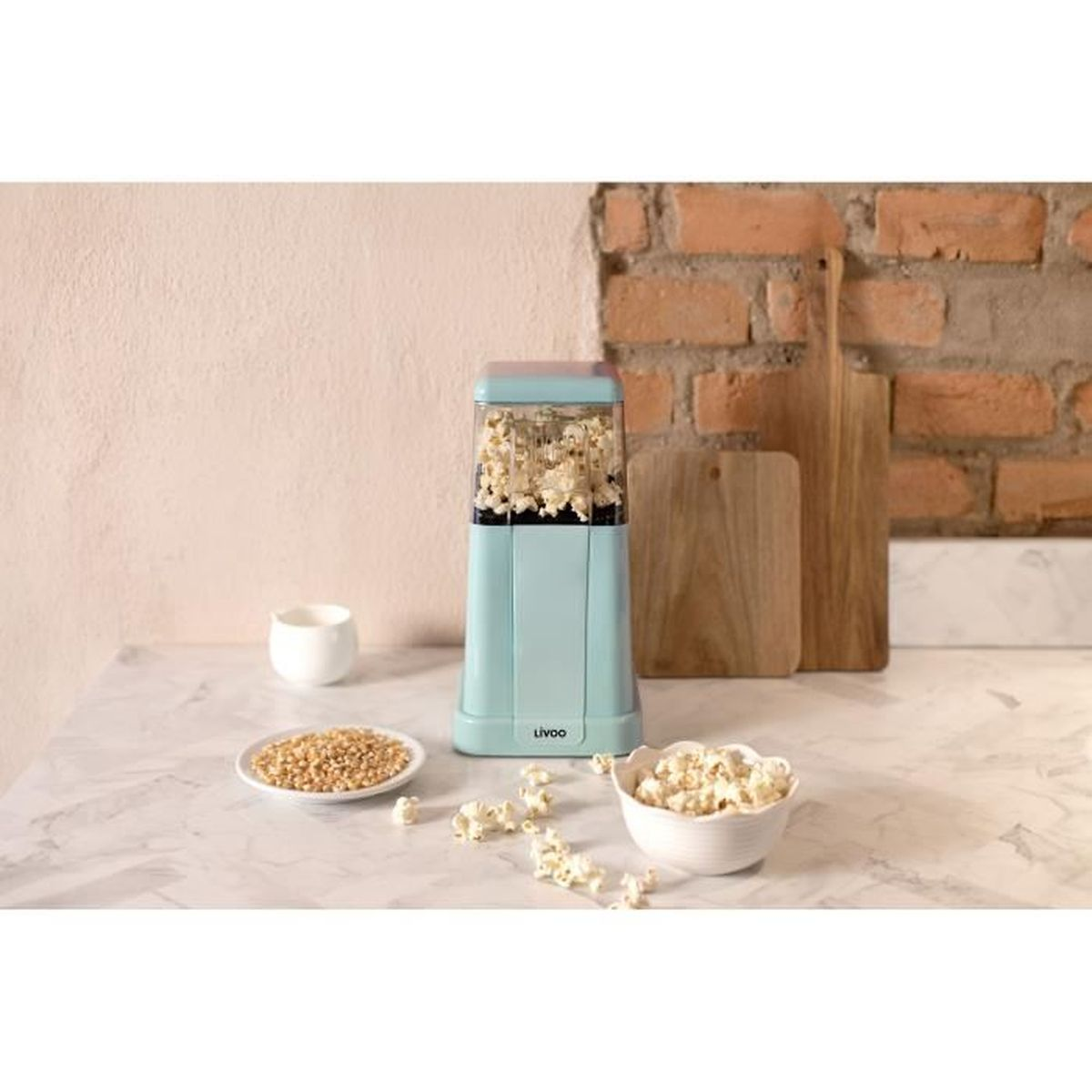 Türkisfarbene Popcornmaschine mit Popcorn, umgeben von Kernen und einer Schüssel Popcorn.