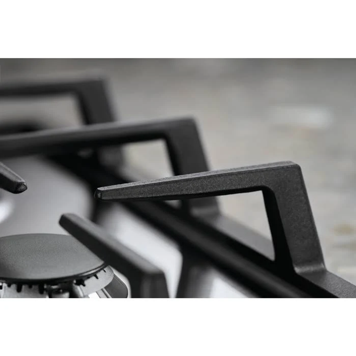 Zbliżenie rusztów palnika kuchenki gazowej. Ruszty są czarne i metaliczne.