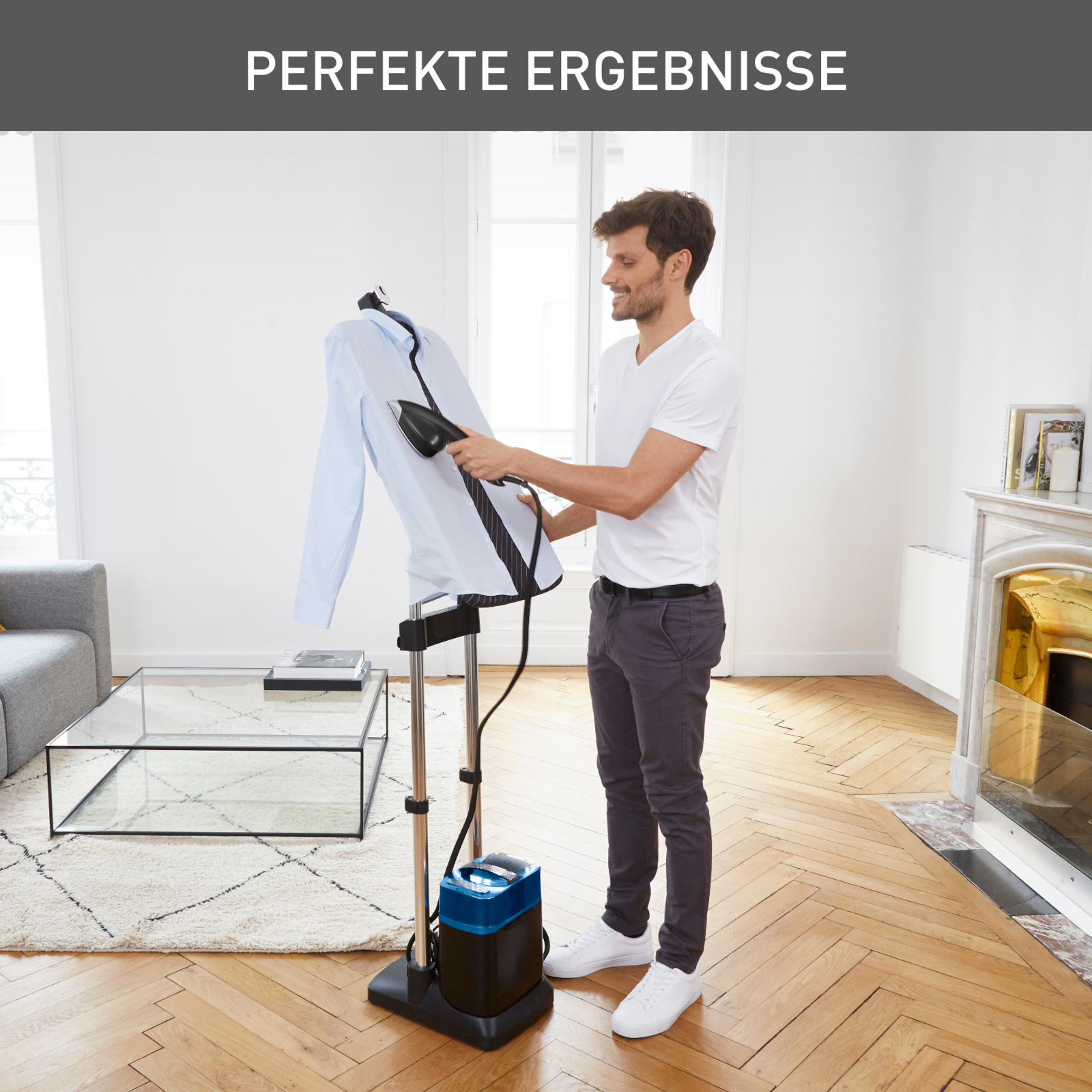 Ein Mann, der ein blaues Hemd auf einem Kleiderdämpfer bügelt. Der Raum hat Holzböden und einen Kamin.