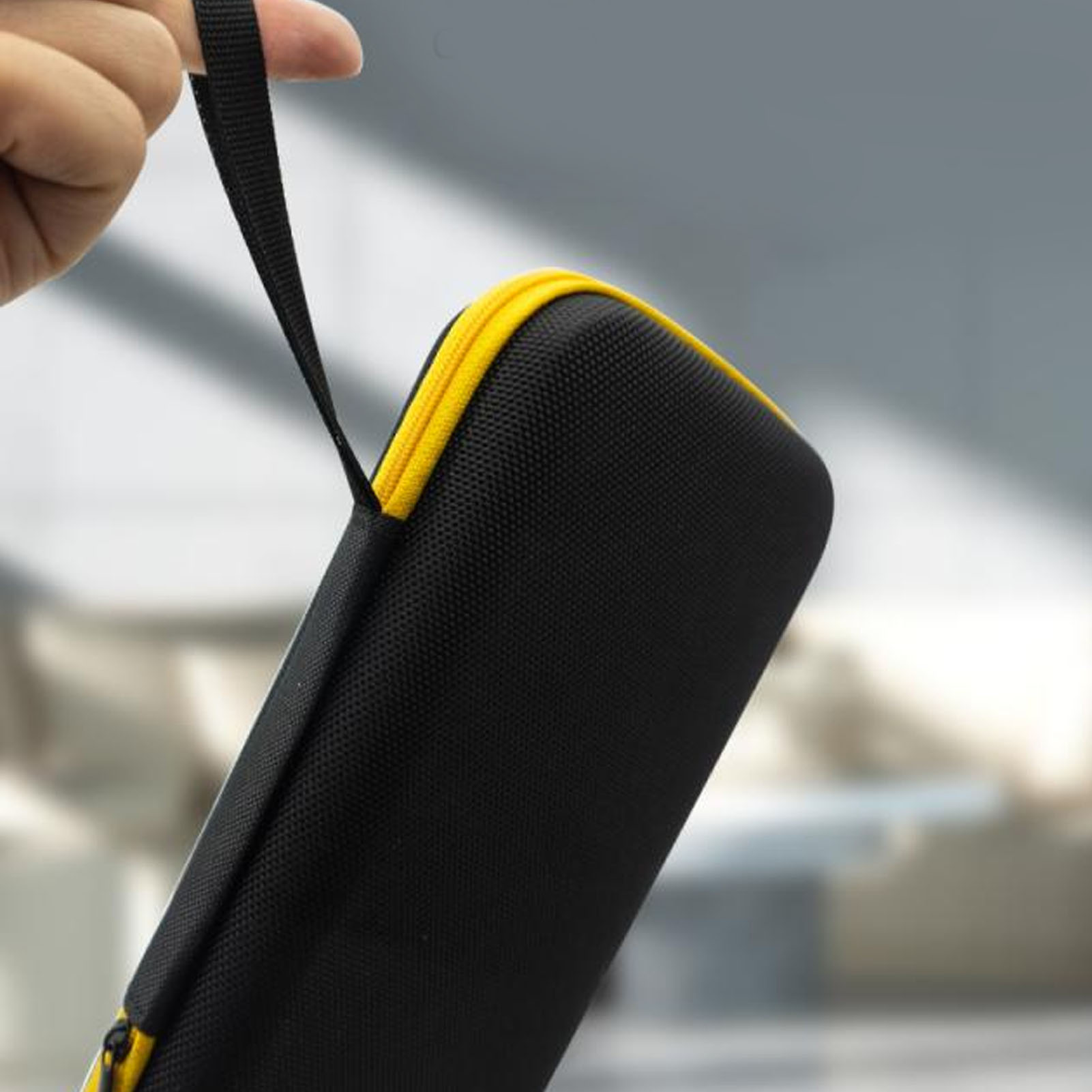 Schwarzes und gelbes Etui mit Griff, das von einer Hand gehalten wird. Der Hintergrund ist unscharf.