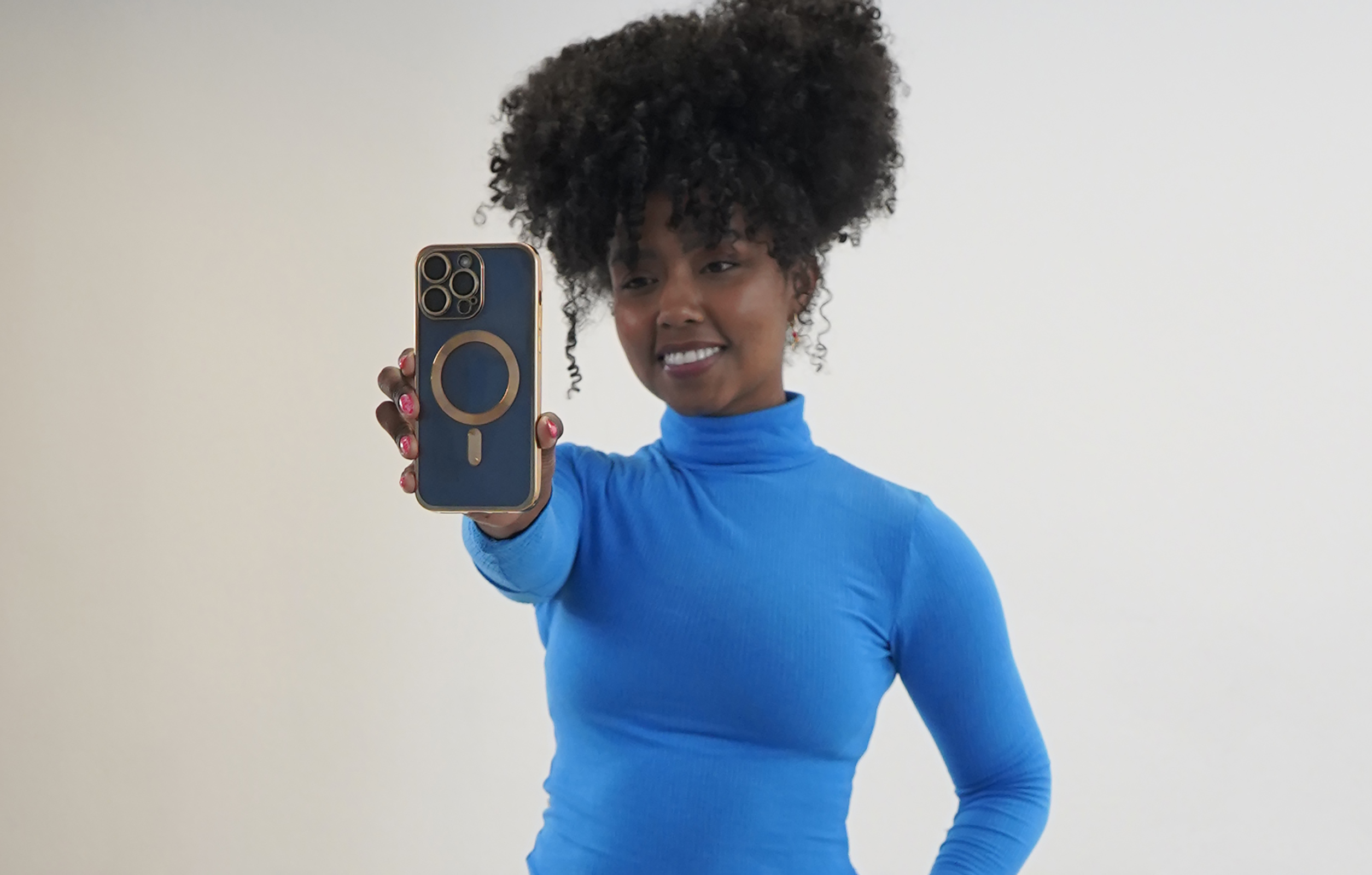 Eine Frau in einem blauen Rollkragen hält eine blaue Handyhülle auf Weiß.