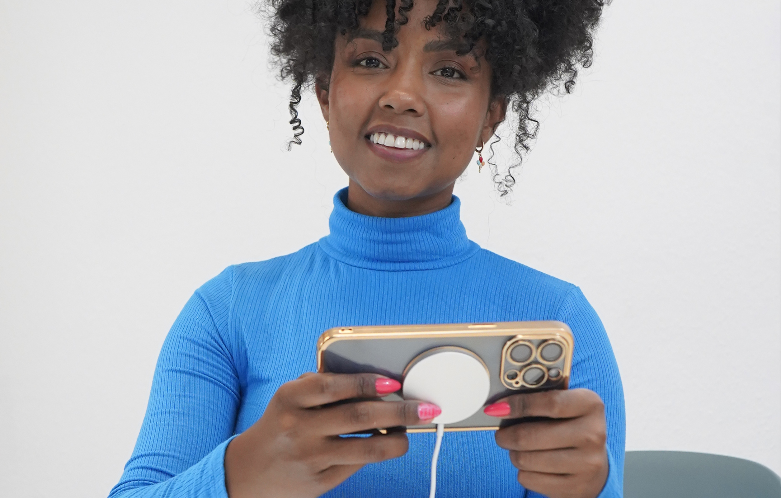 Eine Frau in einem blauen Rollkragenpullover lächelt, während sie ein Telefon mit Ladegerät hält.