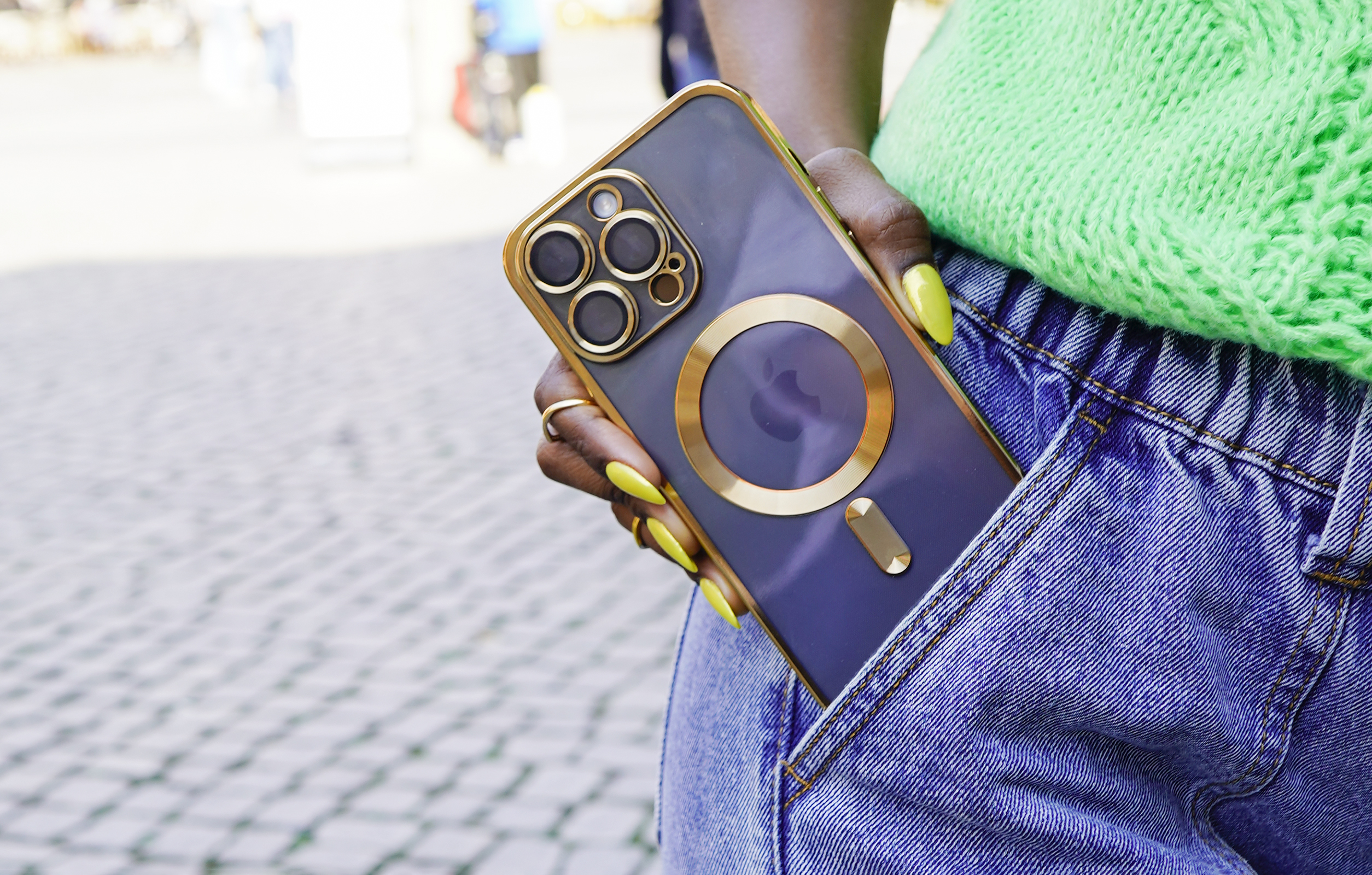 Person hält Telefon mit goldener Hülle in der Tasche, gelbe Nägel.