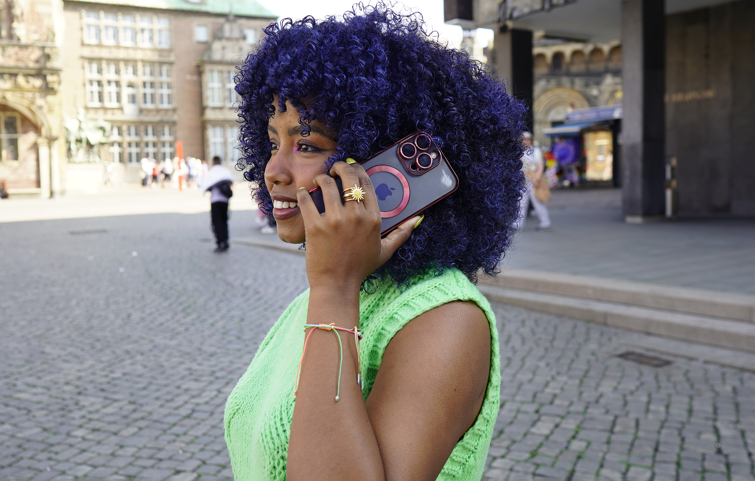 Frau telefoniert, lila Haare und grüne Weste. Hält Telefon mit rotem Kreis auf der Hülle.