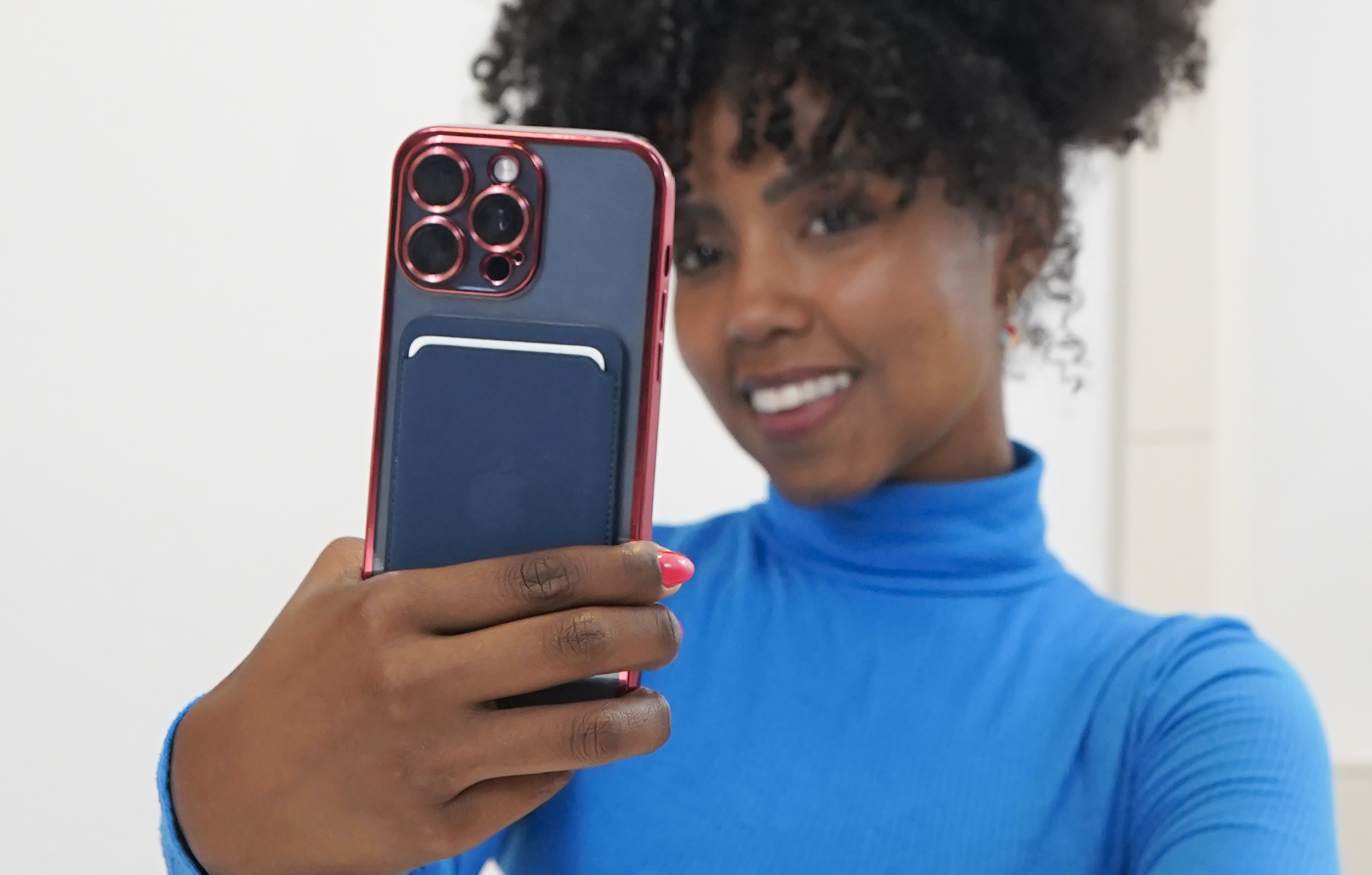 Eine Frau macht ein Selfie mit einem Telefon in einer roten Hülle. Weißer Hintergrund.