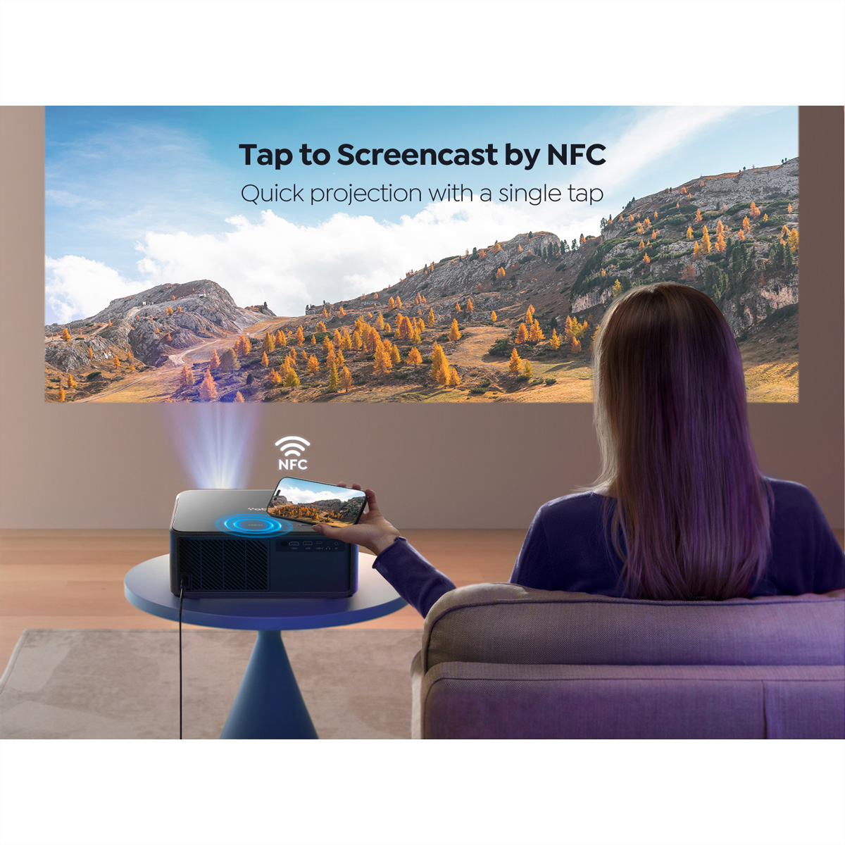 Kobieta używa telefonu do projekcji na ekranie. Projektor, ekran z krajobrazem. Niebieski stół, sofa.