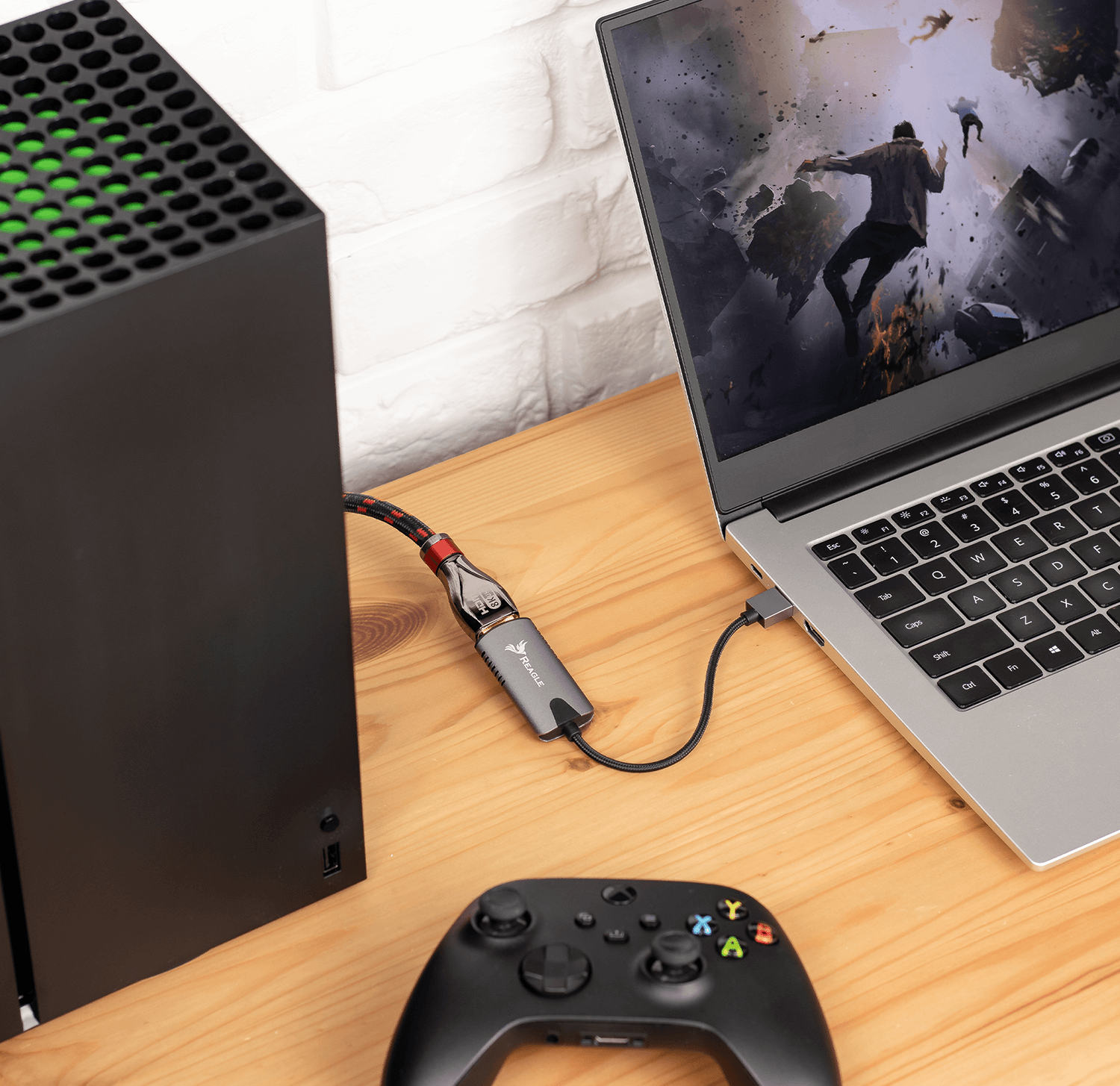 Konfiguracja do gier: konsola, kontroler i laptop wyświetlający scenę z gry, wszystko na drewnianej powierzchni.