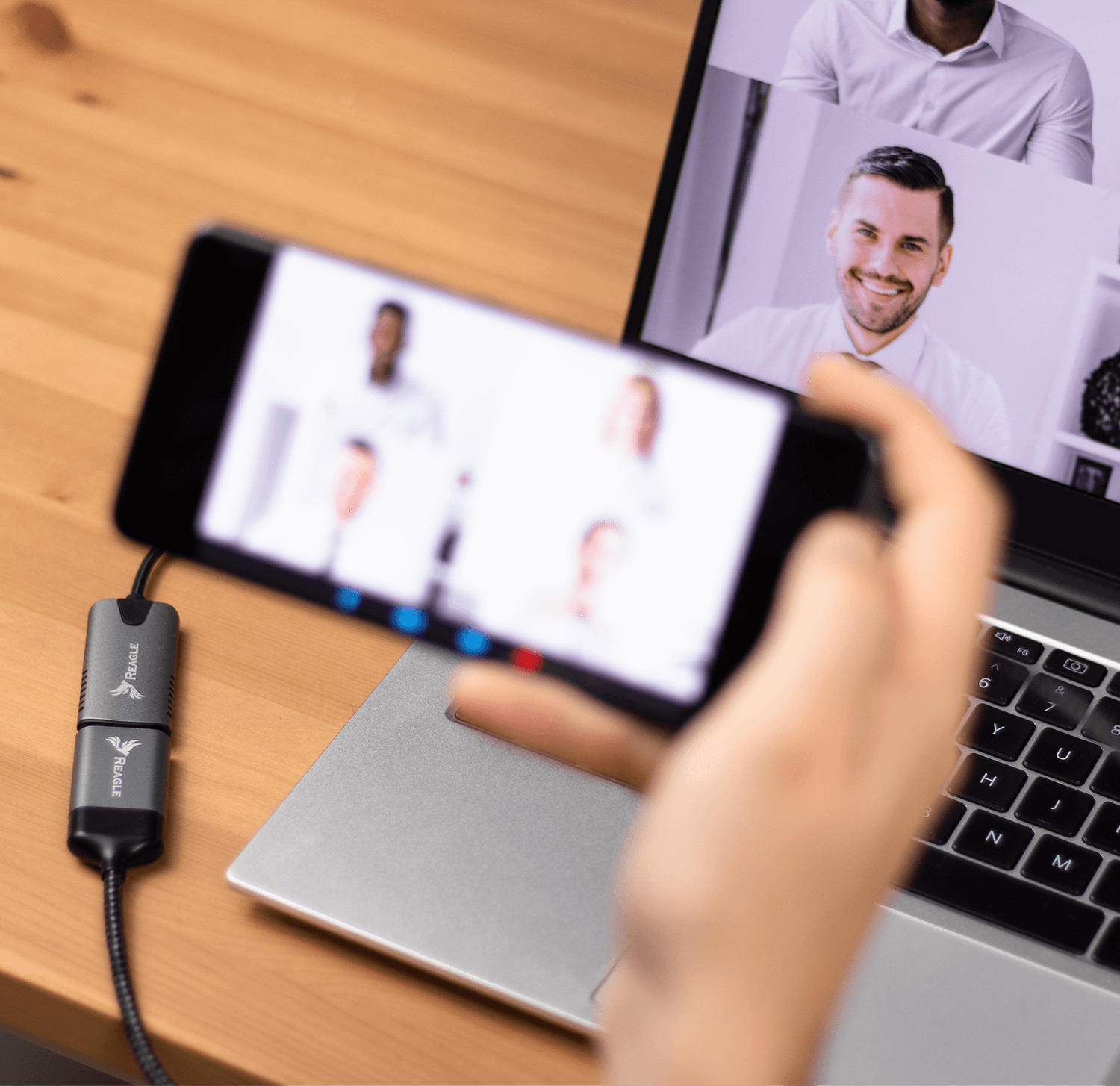 Osoba trzymająca smartfon z rozmową wideo, podłączony do laptopa.