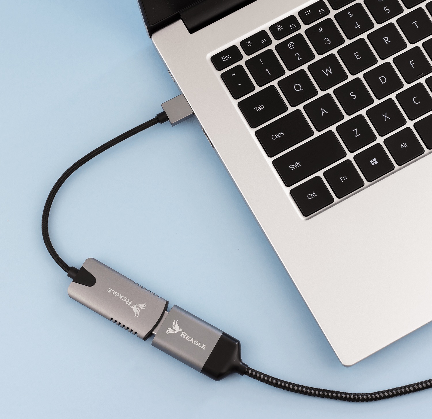 Laptop podłączony do huba USB-C, z logo REAGLE na hubie.