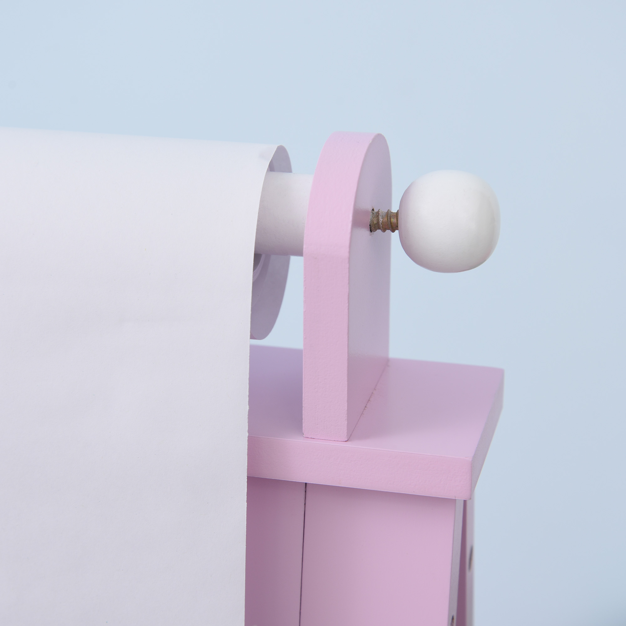 Un portarrollos de papel higiénico rosa y blanco con un rollo de papel, sobre fondo azul claro.