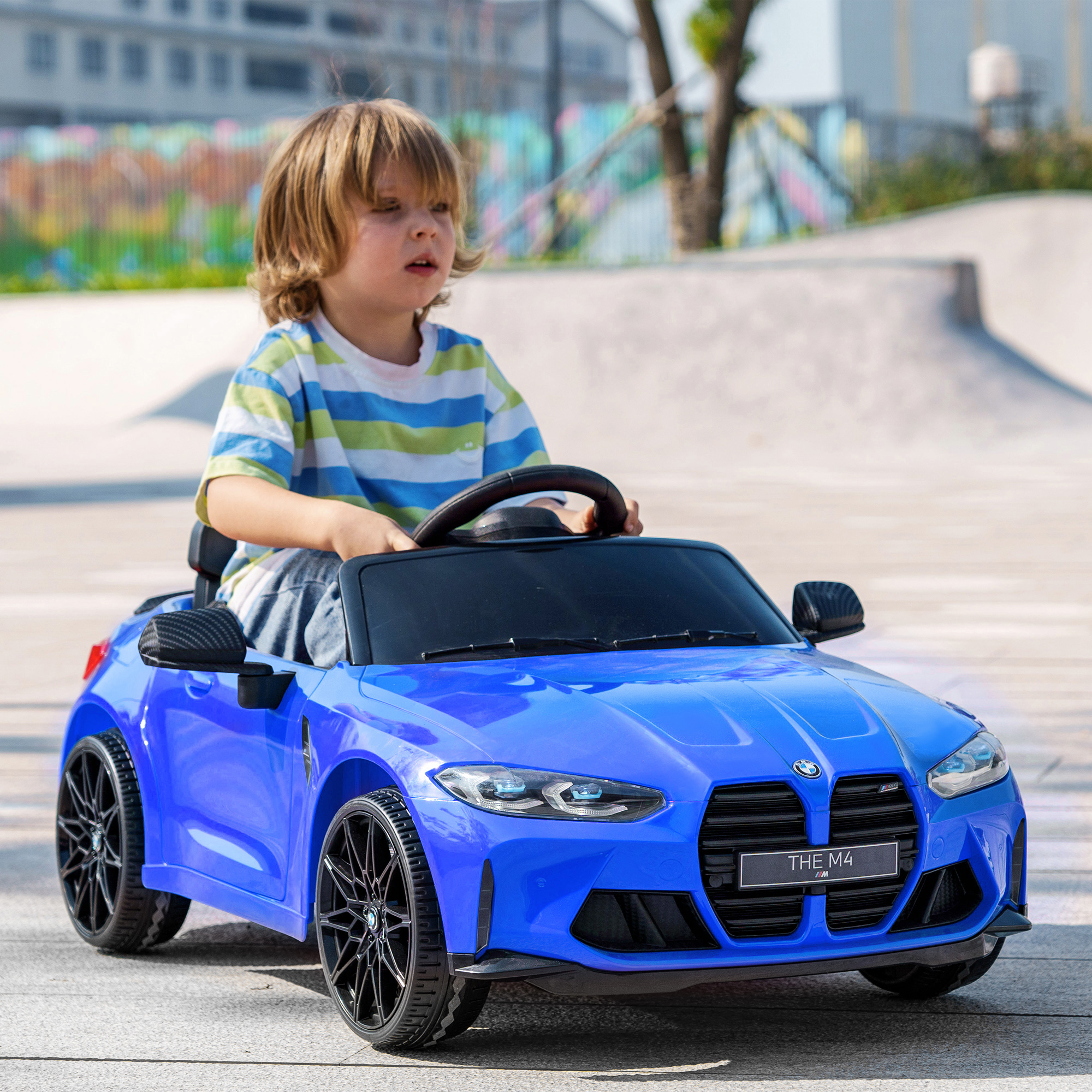 Un niño conduciendo un coche de juguete BMW azul al aire libre en un día soleado, en un parque.