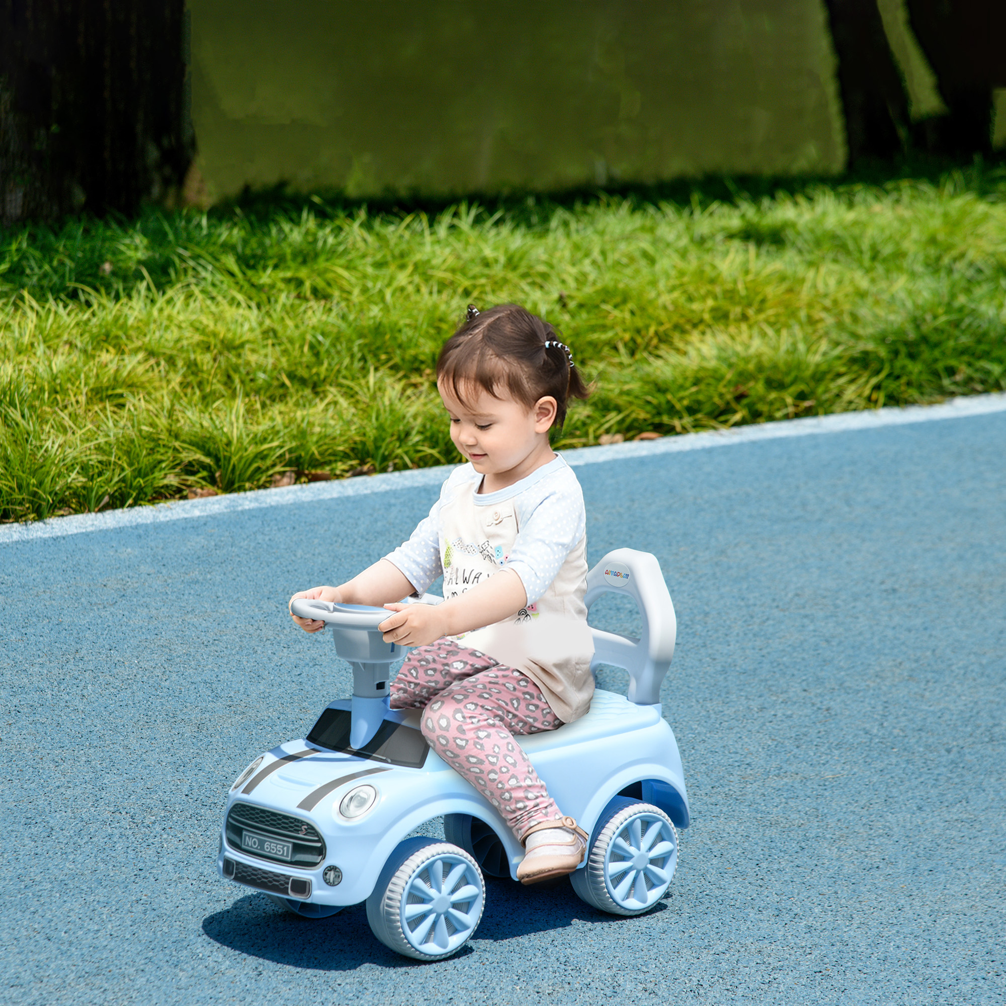 Niña en pantalones rosas conduciendo un coche de juguete azul sobre suelo azul.