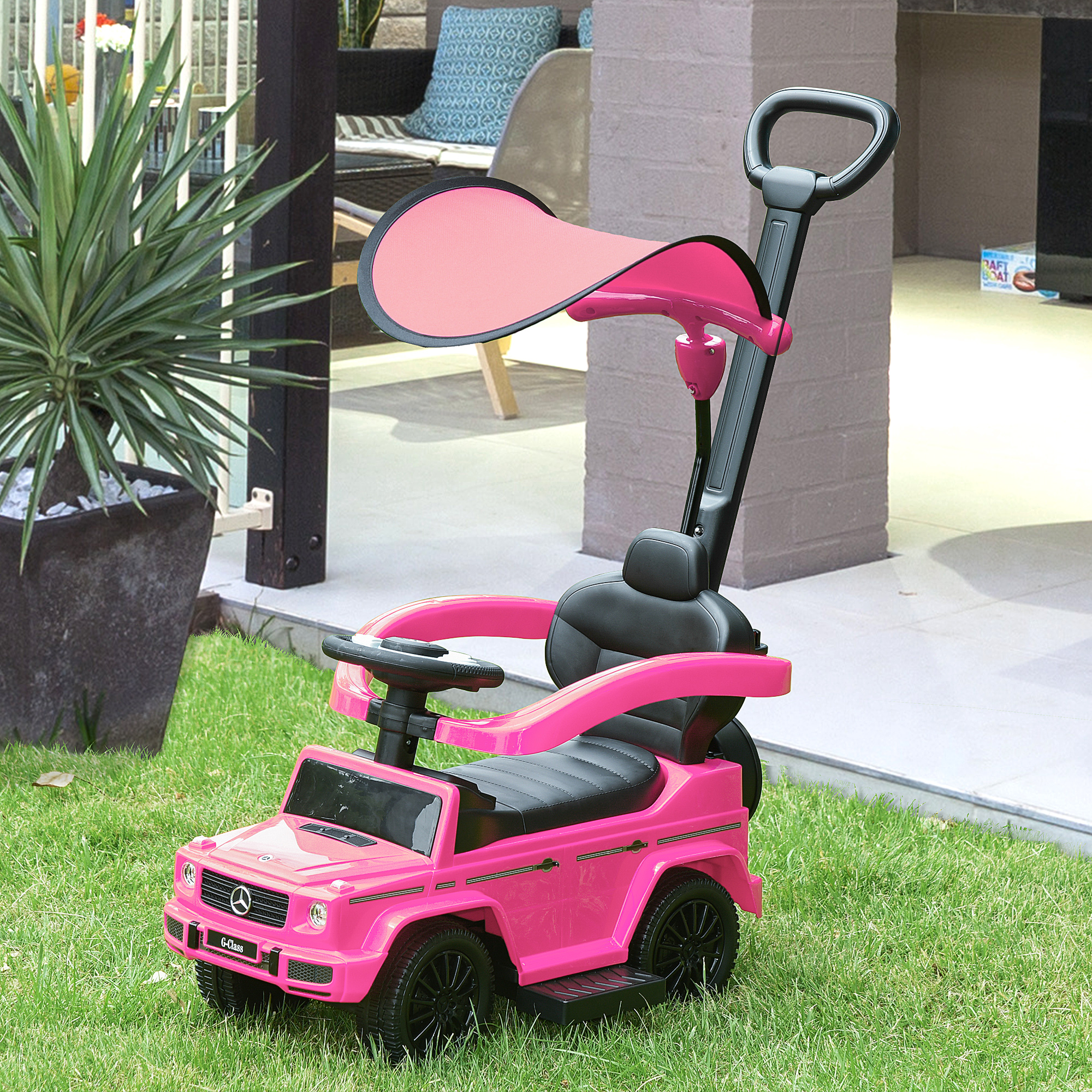 Macchina giocattolo rosa con maniglia, ruote nere e parasole, sull'erba.