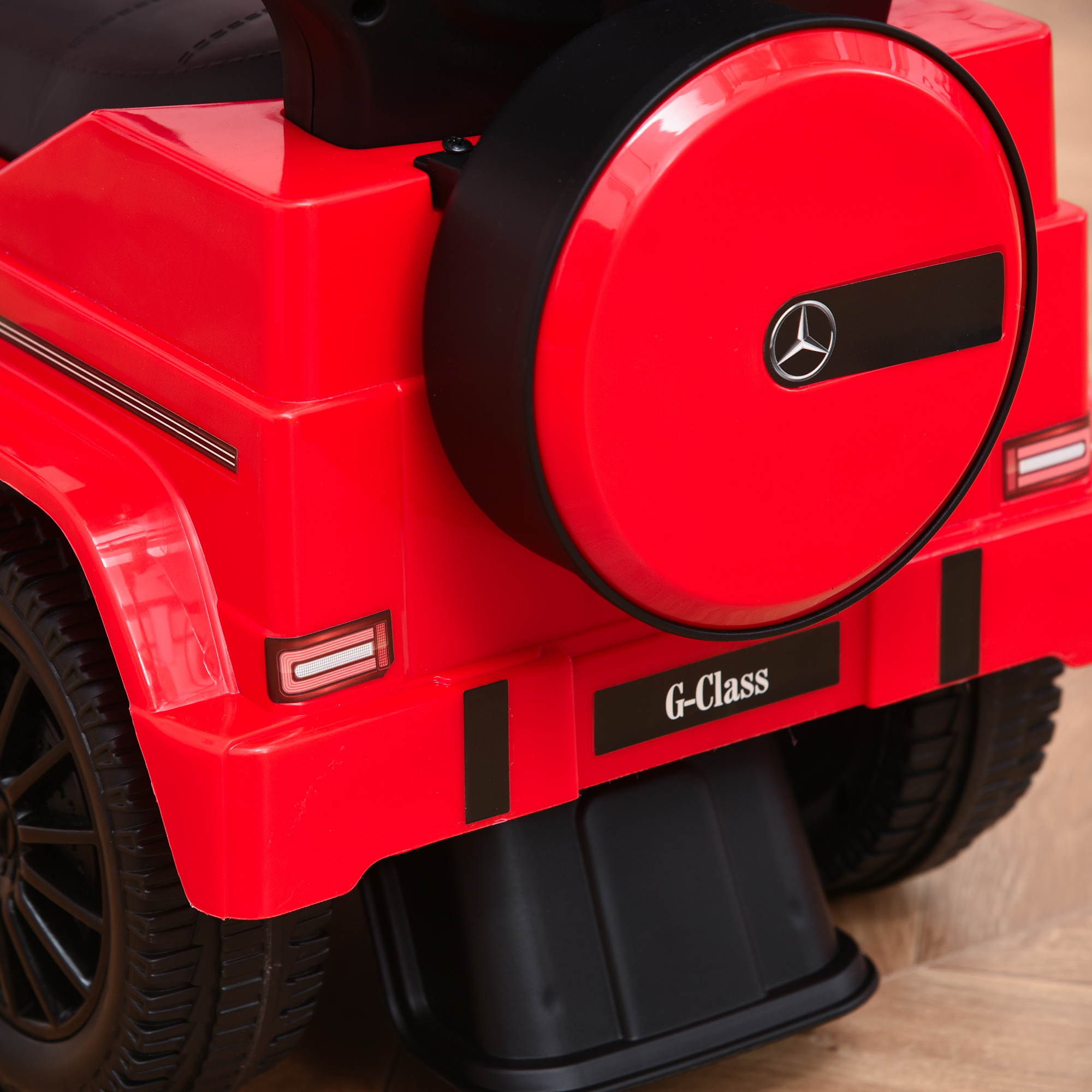 Retro di un'auto giocattolo rossa. Pneumatico nero con copertura della ruota di scorta. Etichetta G-Class. Pavimento in legno.