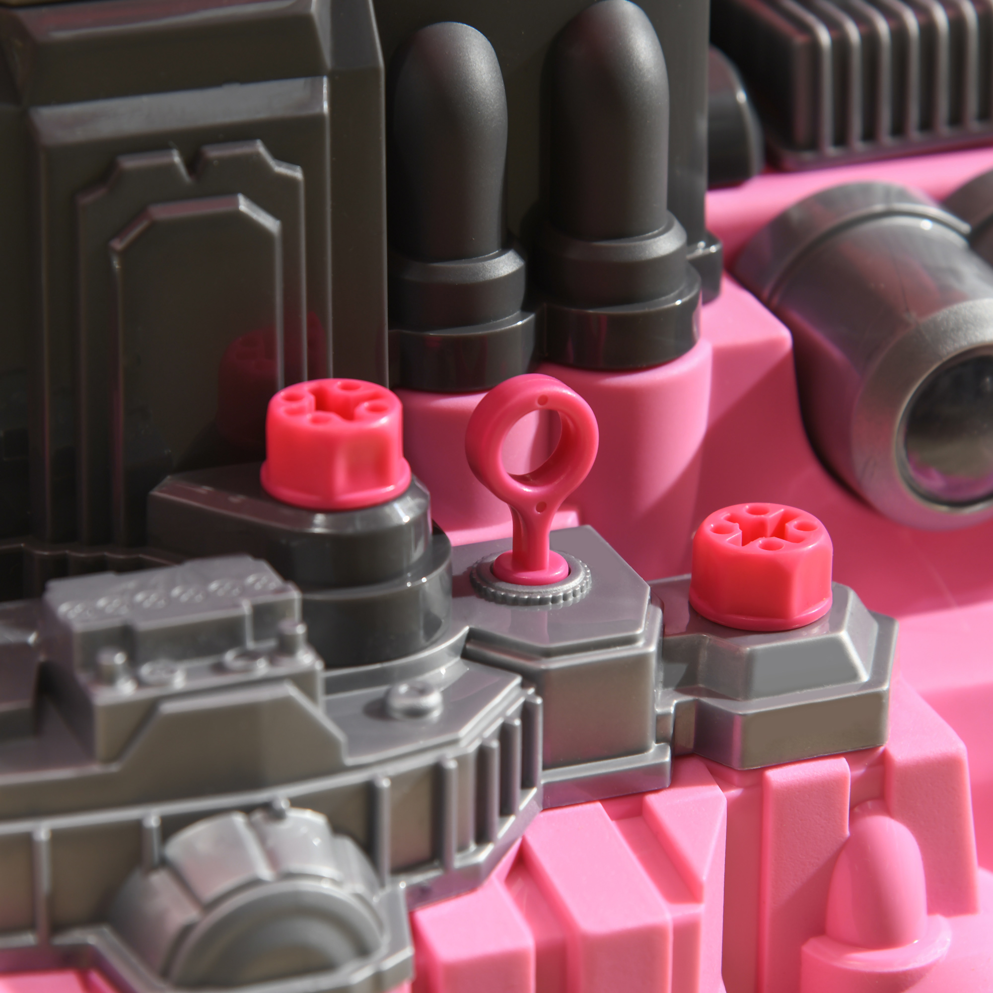 Primer plano de un juguete rosa con detalles grises y botones rojos.
