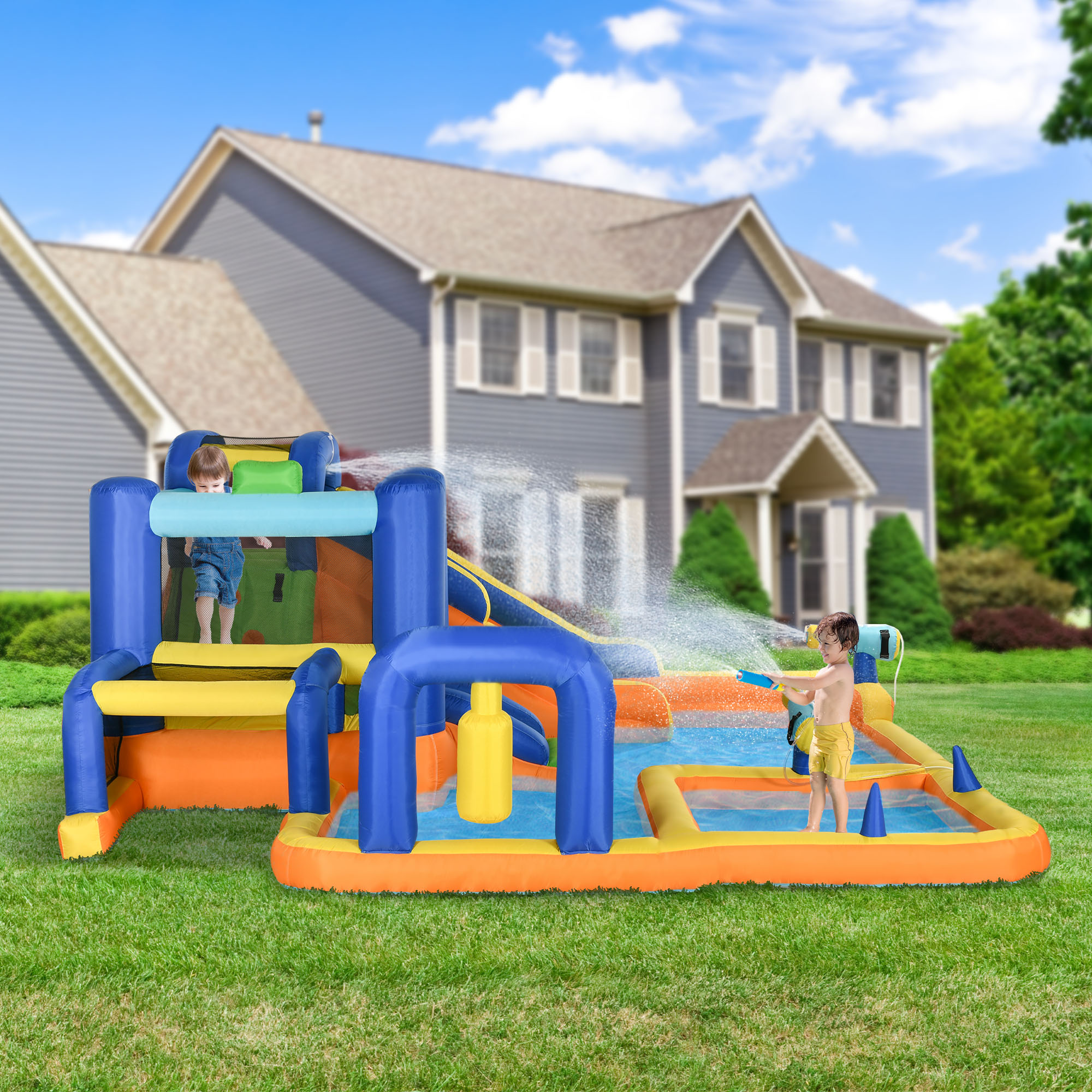 Niños jugando en parque acuático inflable con tobogán y aspersores. Casa y césped al fondo.