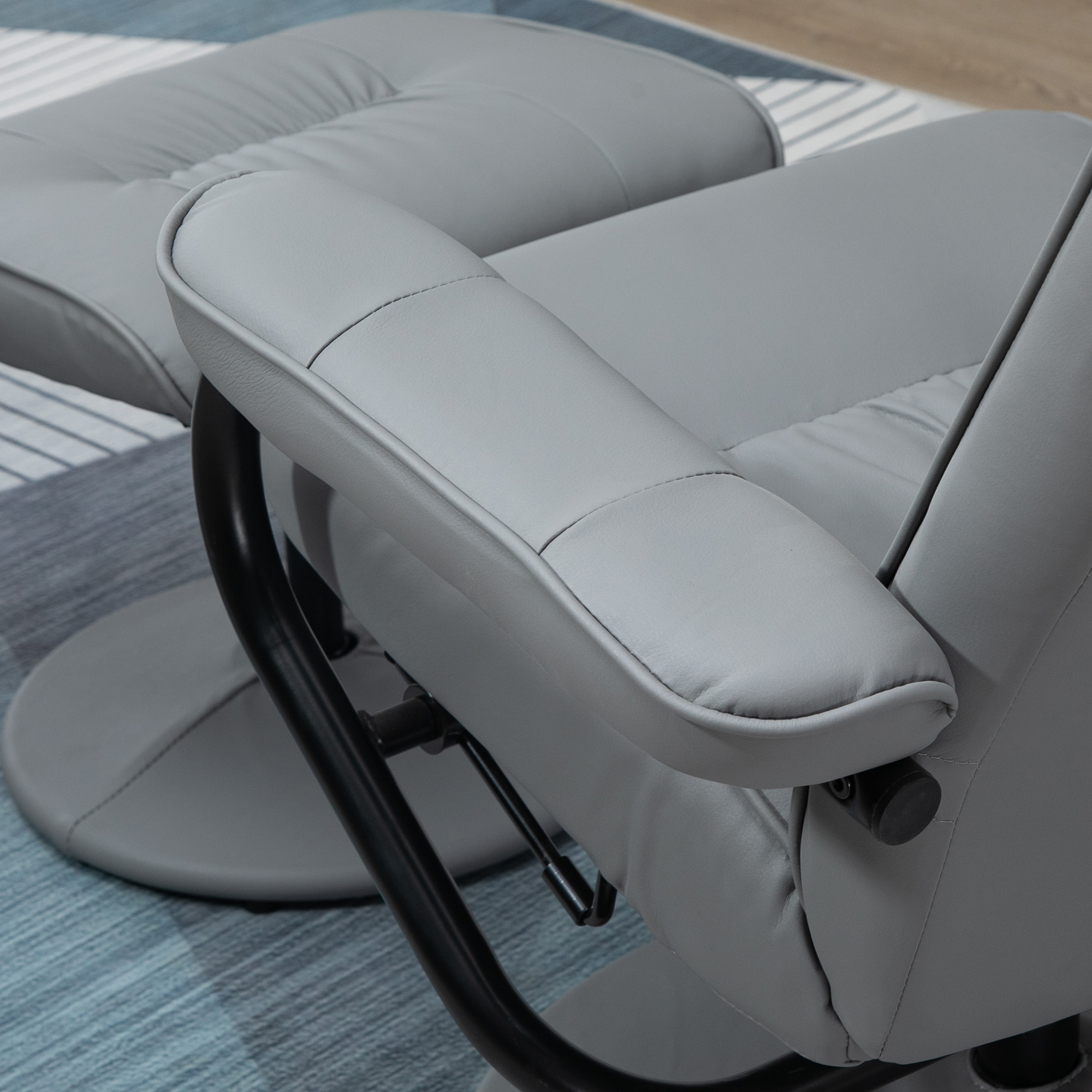 Sillón reclinable gris con reposapiés sobre una alfombra con estampado azul y blanco. Vista de cerca.