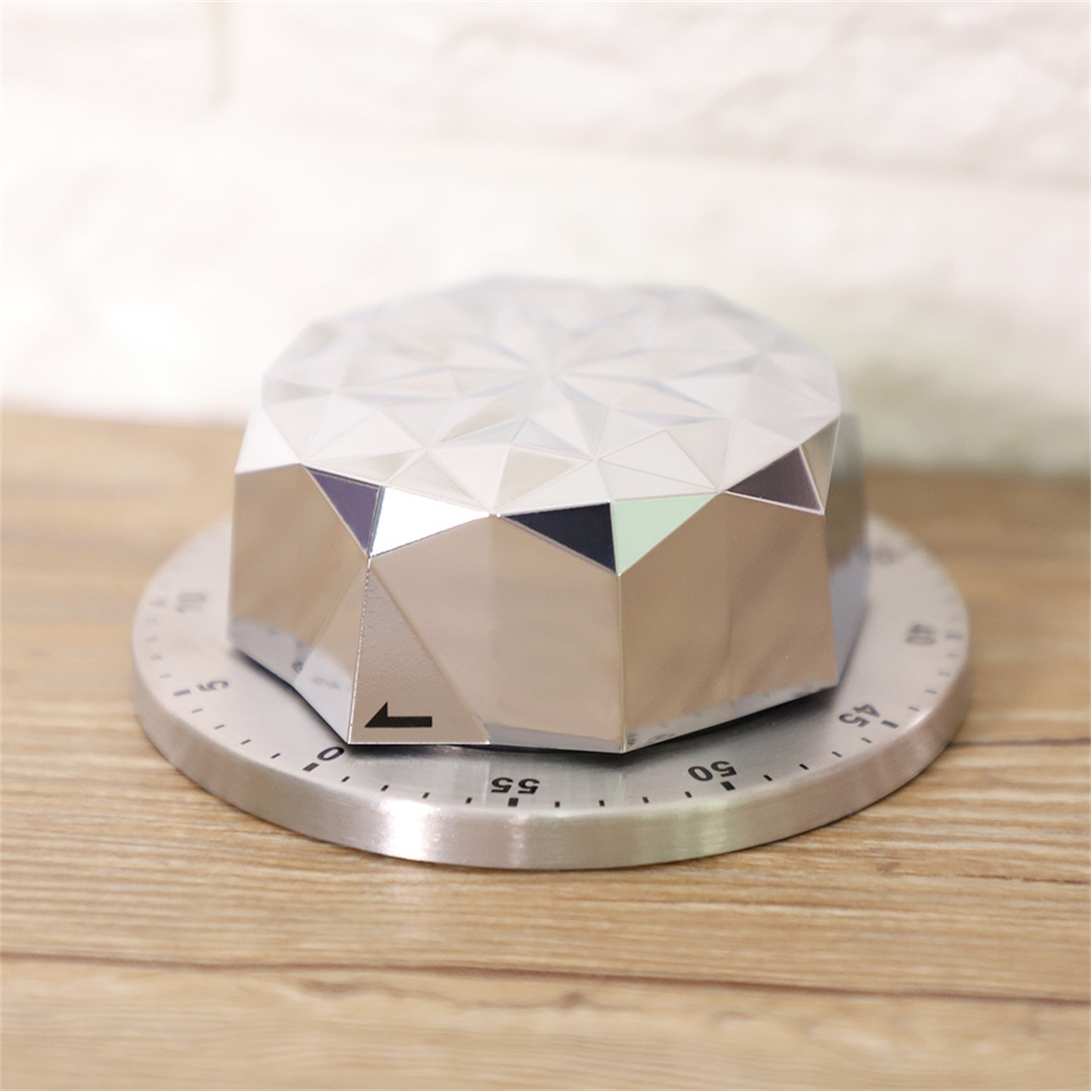 Ein silberner geometrischer Timer auf einem silbernen Sockel. Er steht auf einer Holzoberfläche, mit weißem Hintergrund.