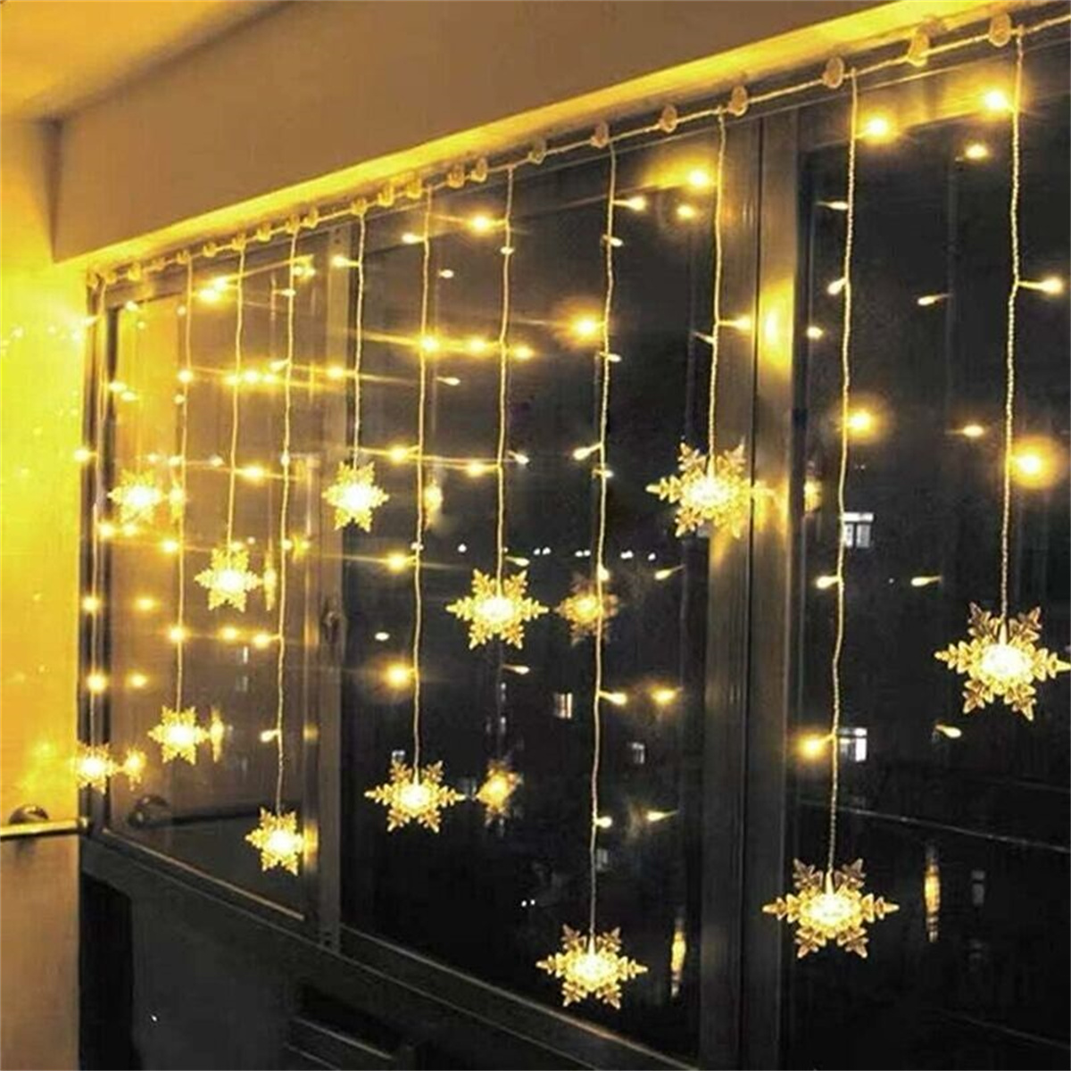 Ein Vorhang aus schneeförmigen Lichtern, der von einem Fenster hängt und eine dunkle Nacht beleuchtet.
