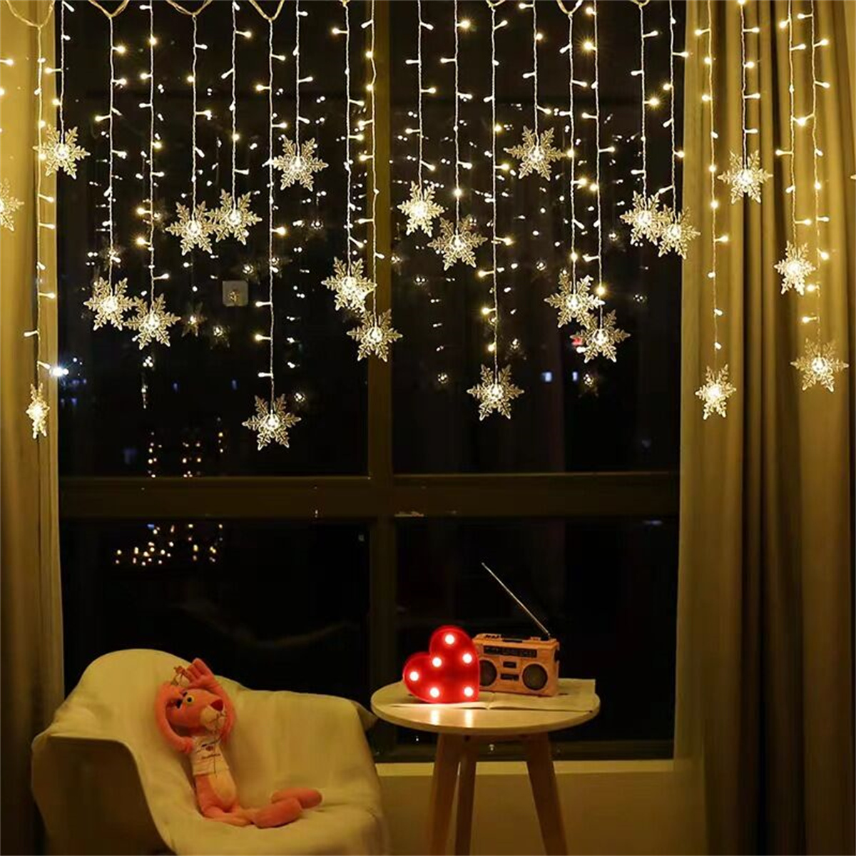 Fenster mit Schneeflockenlichtern, Tisch mit Herzlichtern und ein rosa Teddybär.