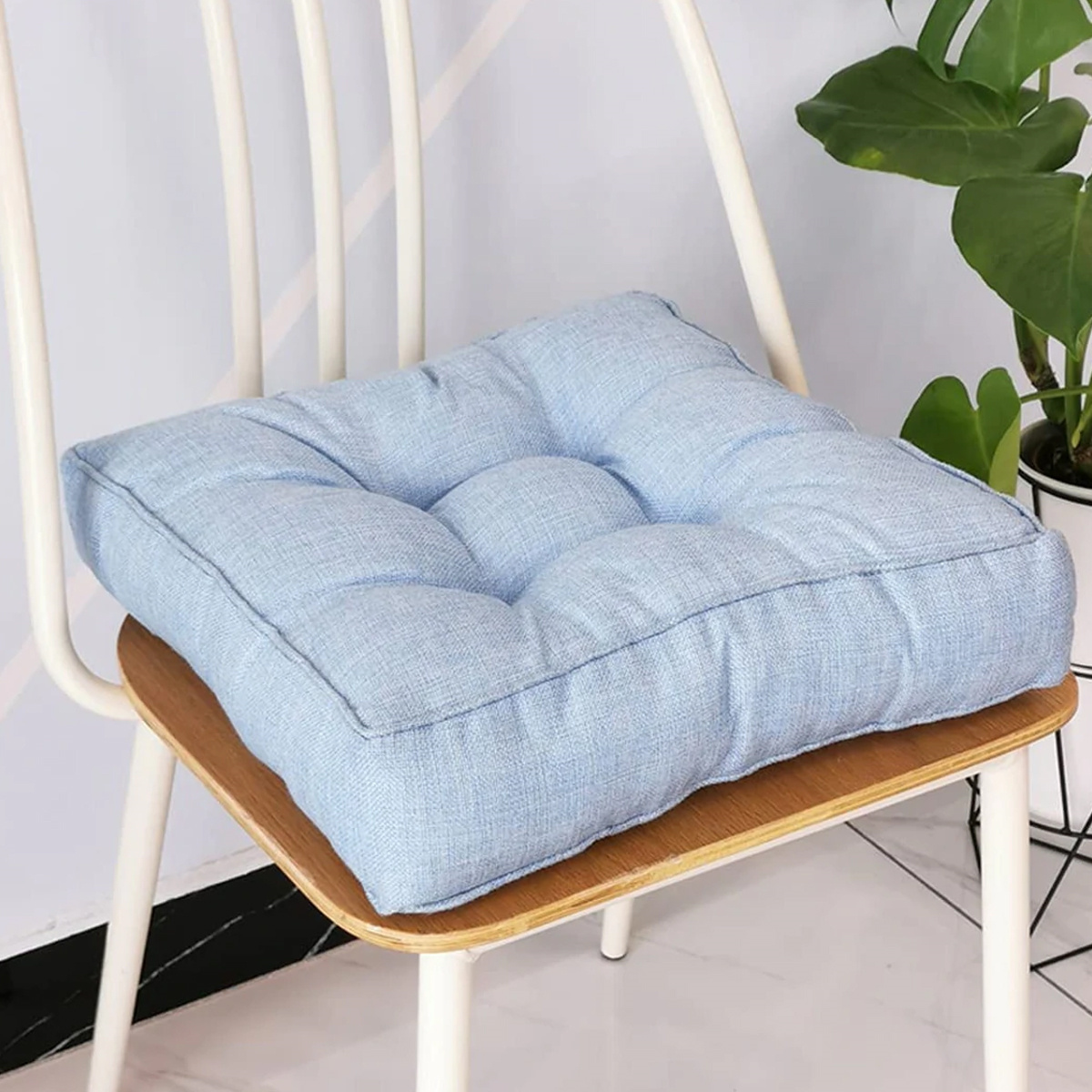 Ein quadratisches, blaues Kissen auf einem Stuhl. Das Kissen hat ein Knopf-Tufting-Design.