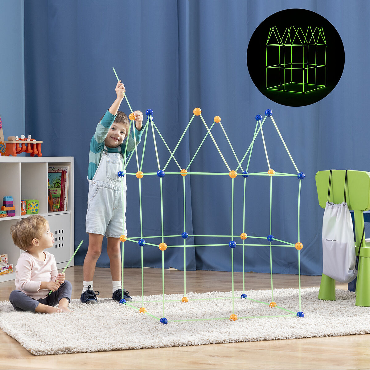 Due bambini costruiscono una struttura con aste verdi e connettori blu su un tappeto bianco.