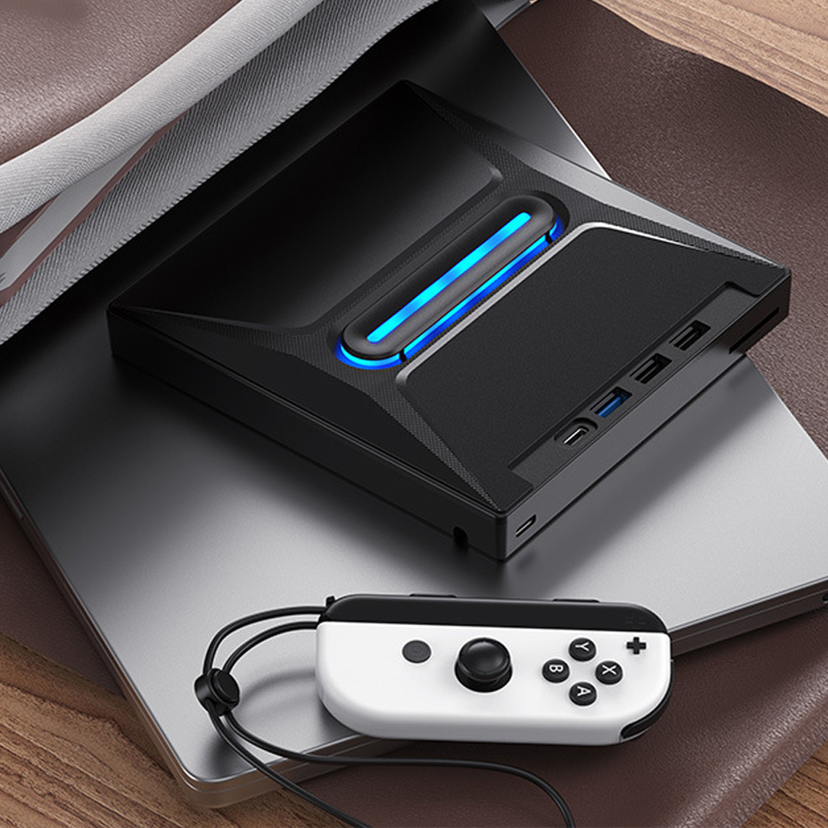 Schwarze Spielkonsole mit Laptop oben drauf. Ein weißer und schwarzer Controller ist vorne.