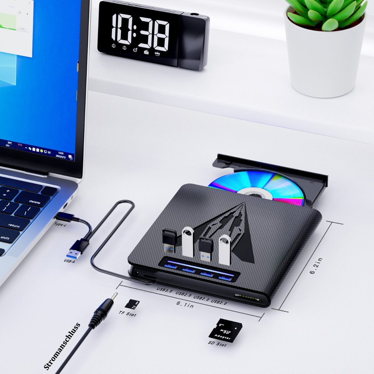 Ein Schreibtisch mit einem Laptop, einem CD-Laufwerk und angeschlossenen USB-Geräten. Eine Uhr befindet sich oben links.