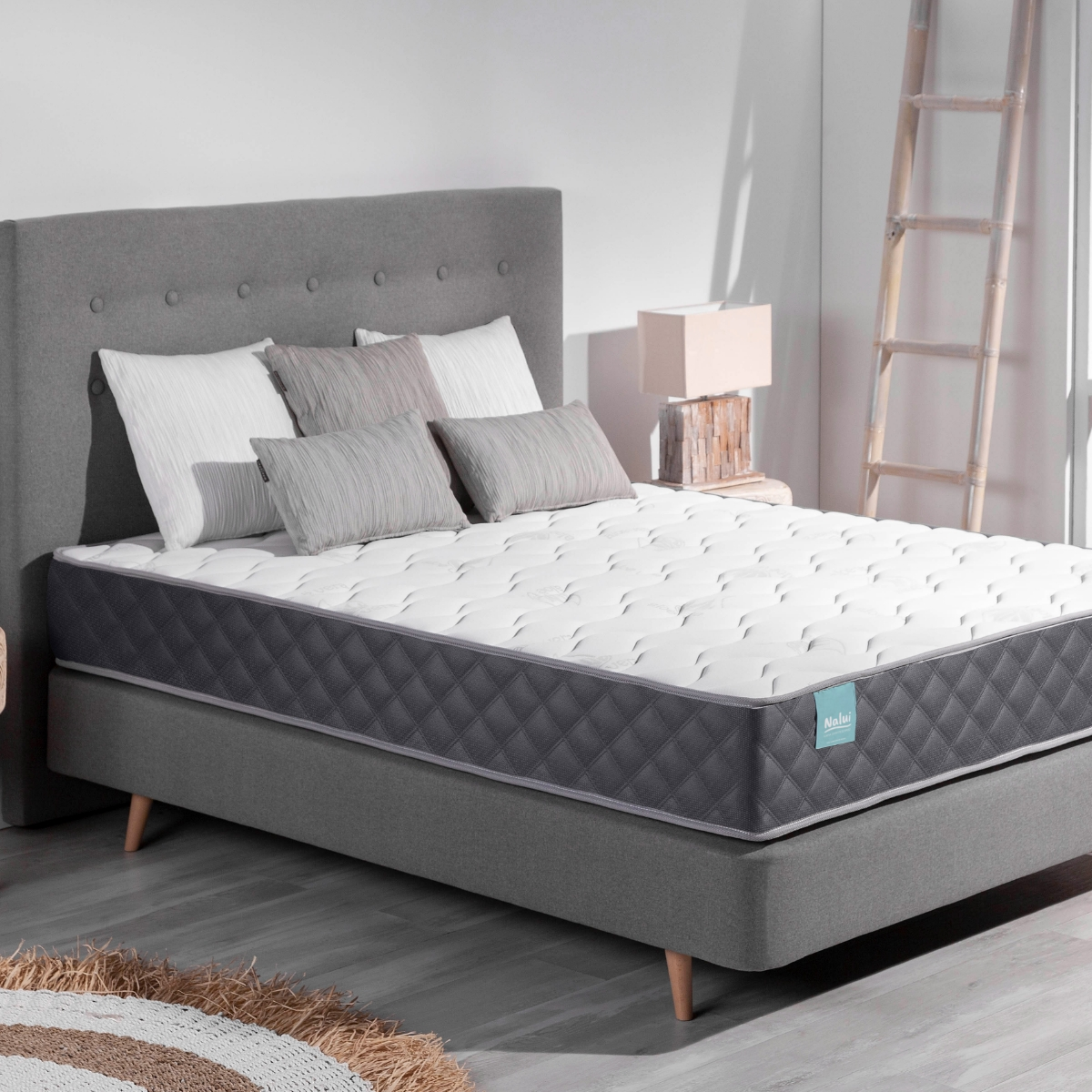 Una cama con cabecero gris, almohadas blancas y un colchón con patrón de diamantes grises, tonos neutros.