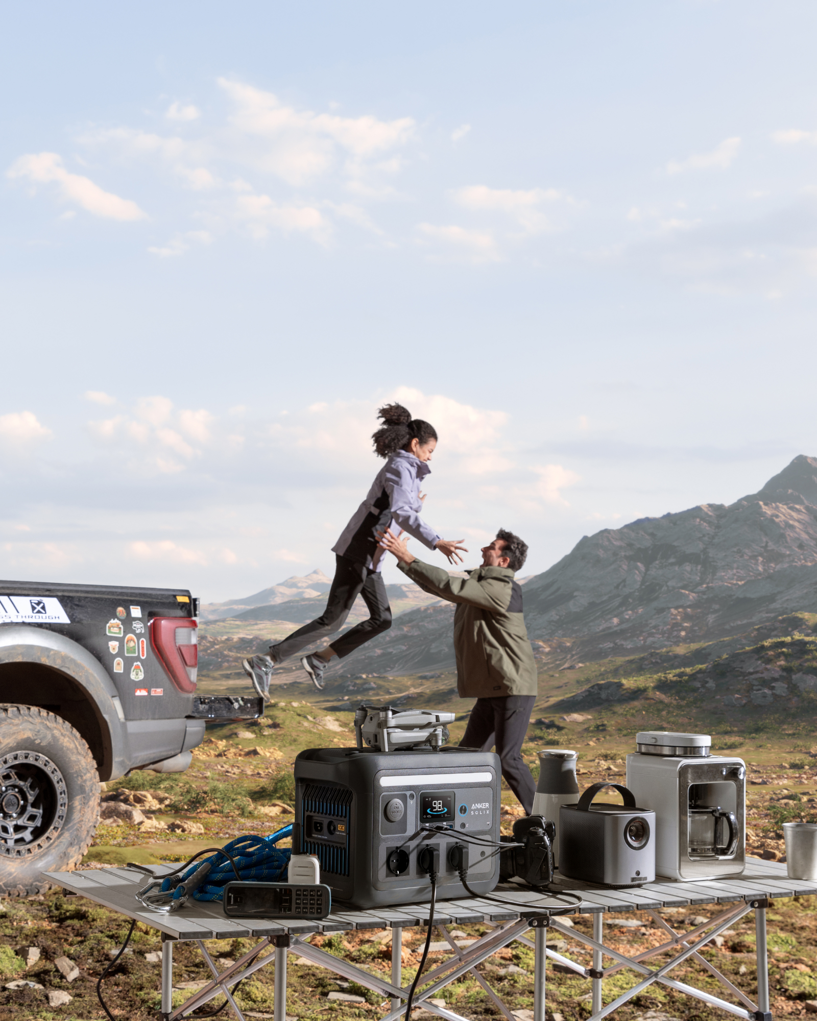 Ludzie bawią się w pobliżu ciężarówki, ze sprzętem kempingowym na stole.