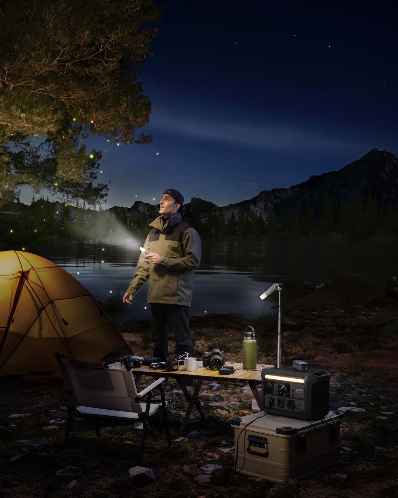 Mężczyzna na kempingu w nocy, z namiotem, stołem i jeziorem w tle.