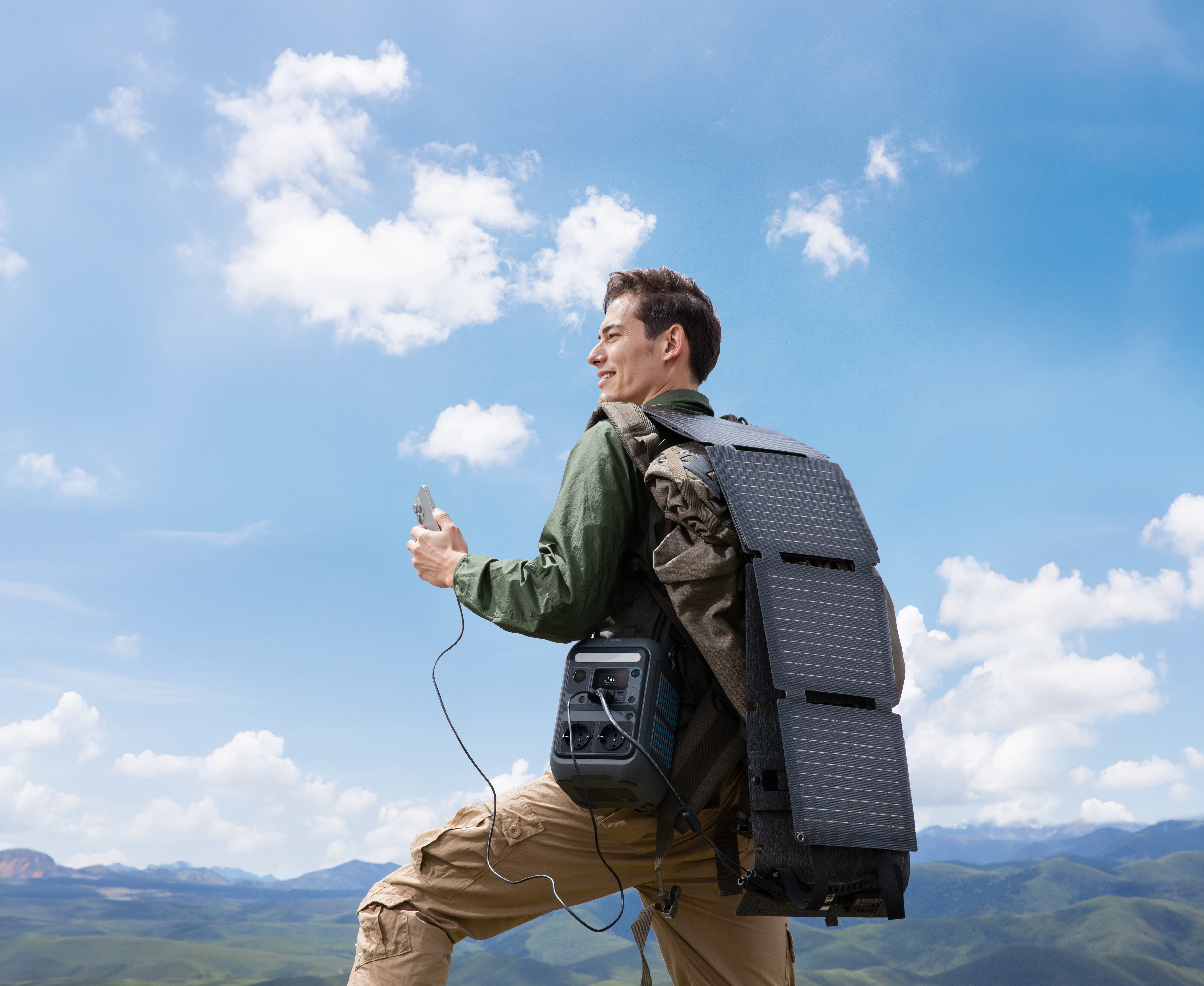 Mężczyzna z plecakiem i panelem słonecznym idzie po górze. Trzyma telefon, a do torby przymocowana jest elektrownia.