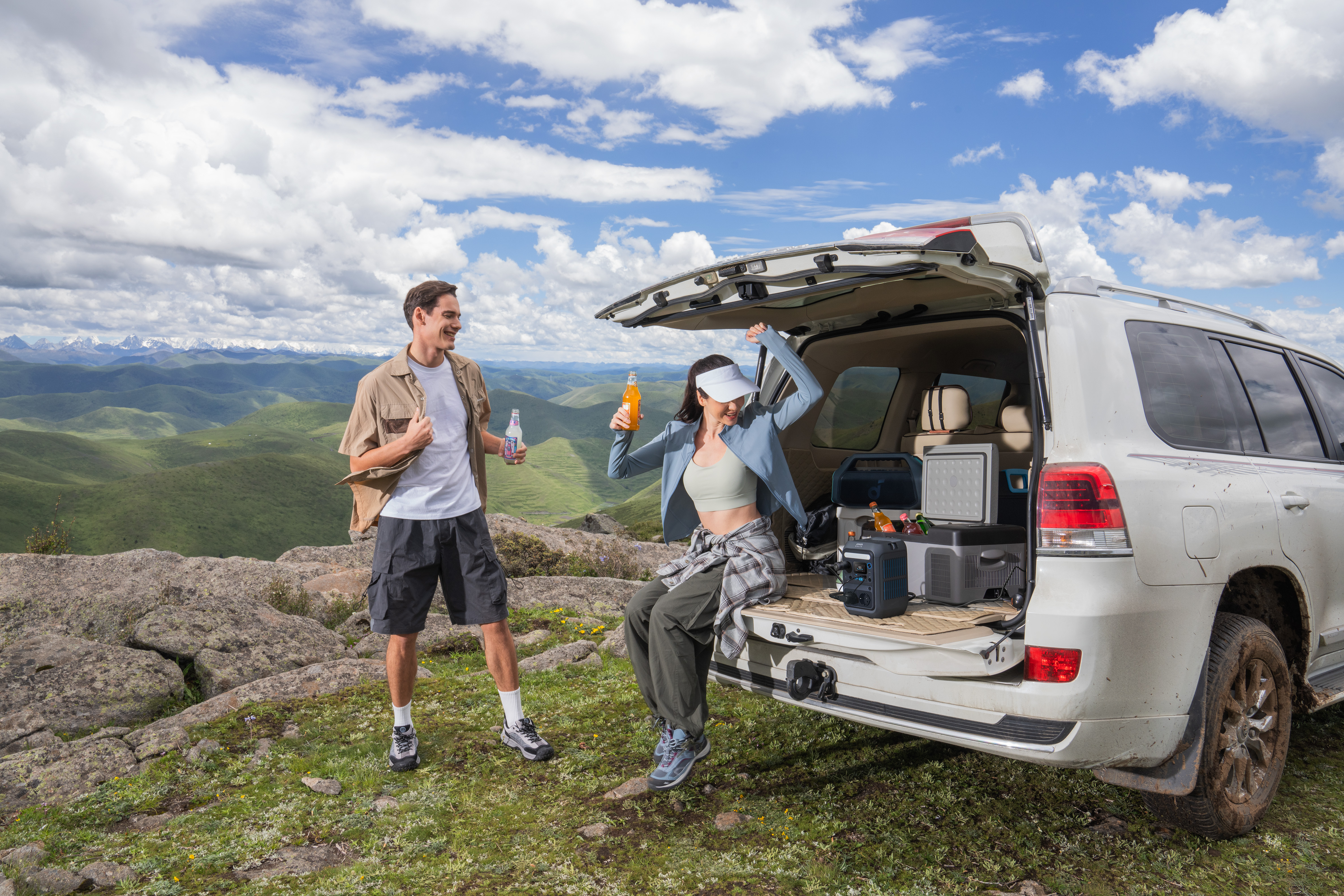 Dwie osoby w pobliżu samochodu z otwartym bagażnikiem na malowniczym szczycie góry.