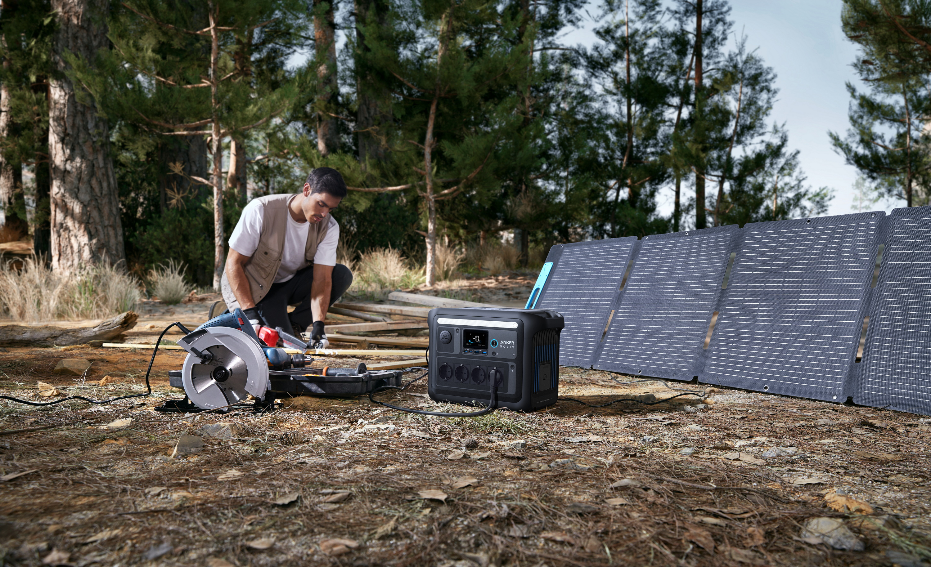 Mężczyzna piłujący drewno piłą tarczową, panele słoneczne i elektrownia w tle.