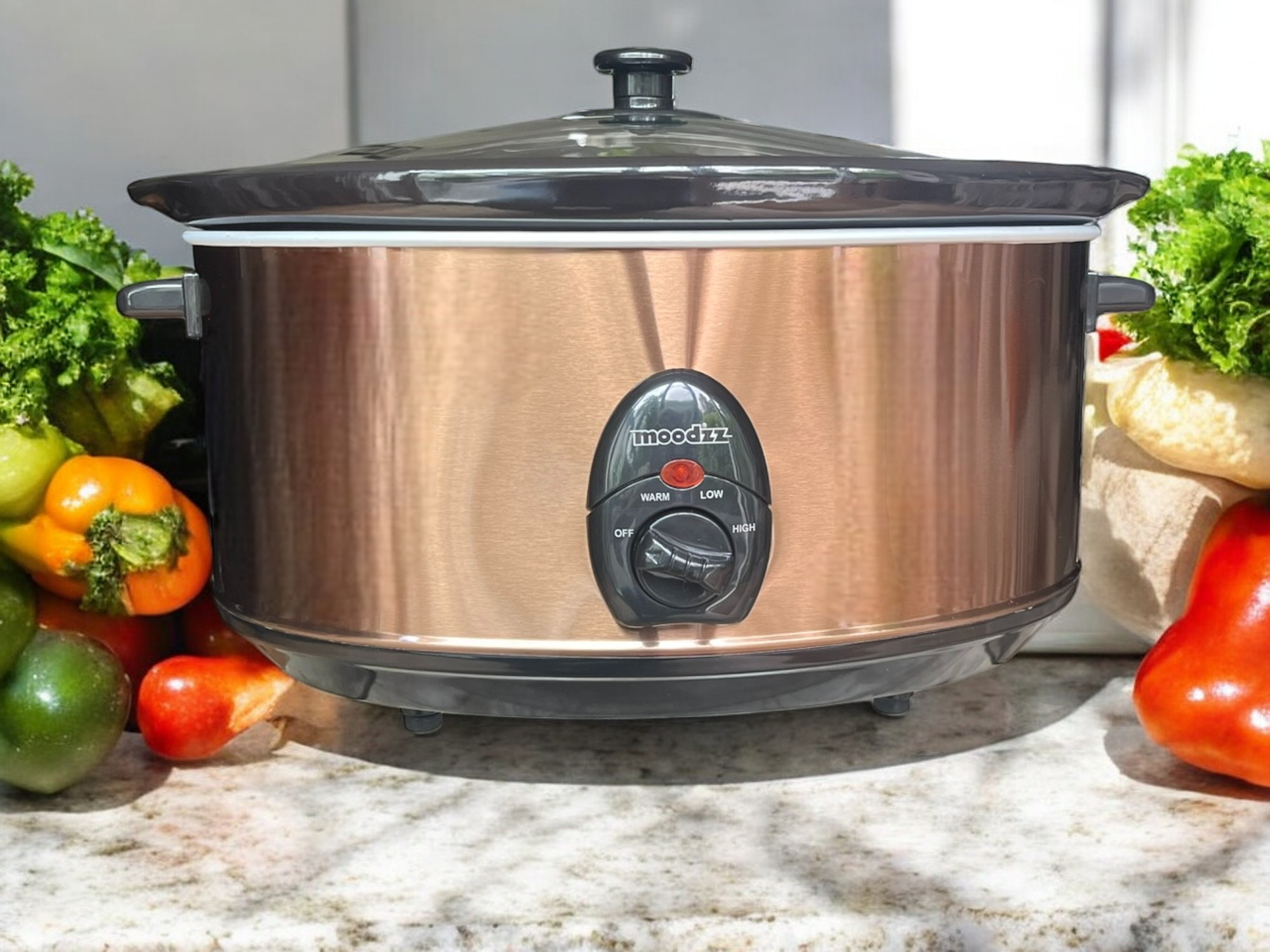 Bronzen slowcooker met groenten eromheen, op een marmeren aanrecht.