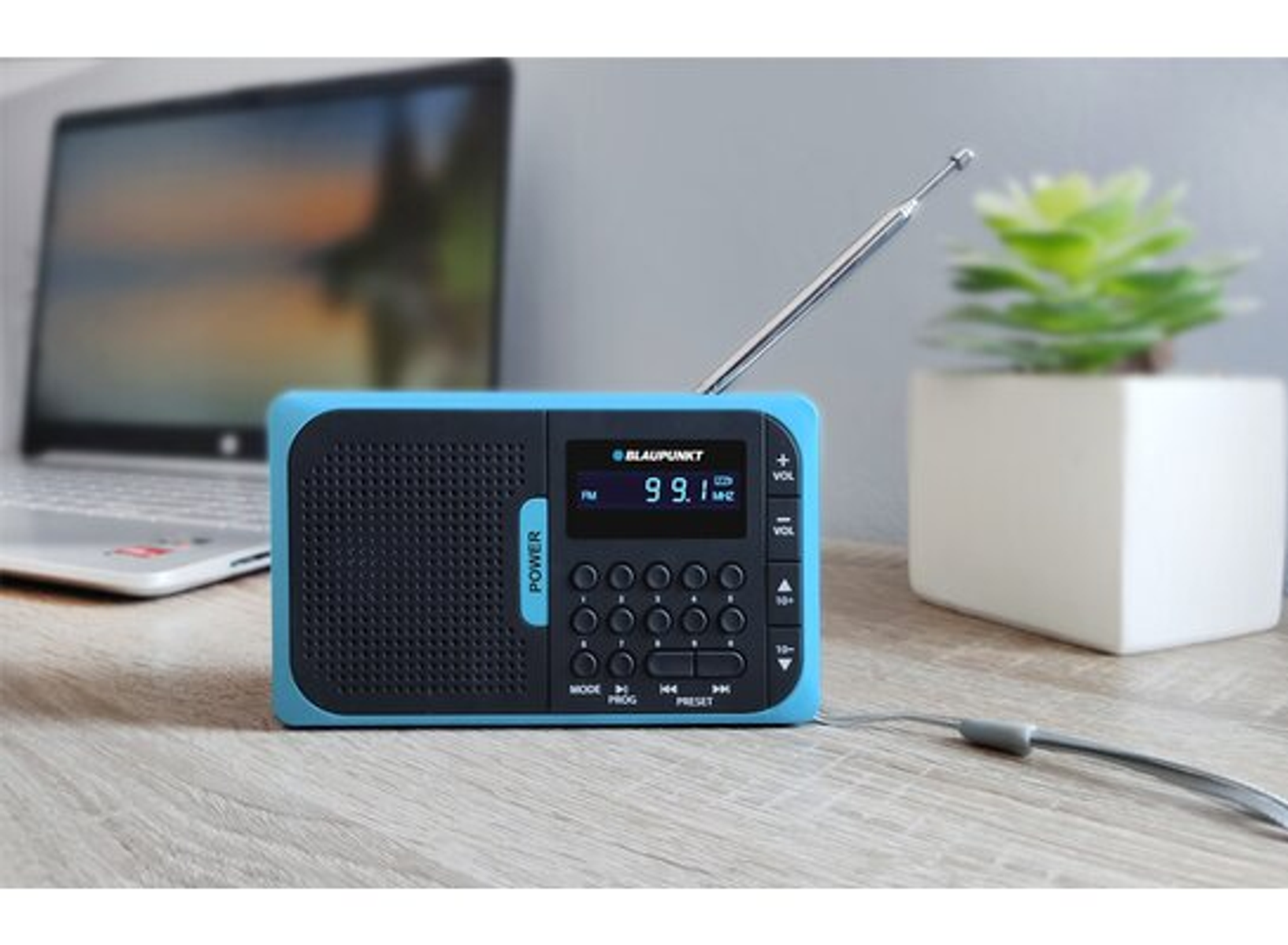 Una radio Blaupunkt blu su una scrivania, con un laptop e un vaso di piante sullo sfondo.