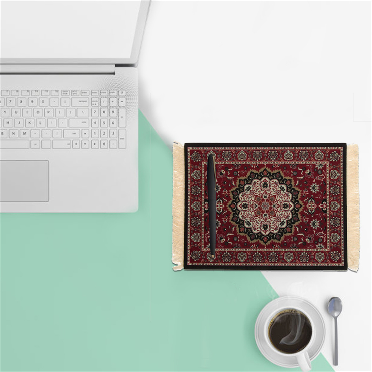 Weißer Laptop, Stift auf roter Teppich-Design-Matte und eine Tasse Kaffee auf einem grün-weißen Schreibtisch.
