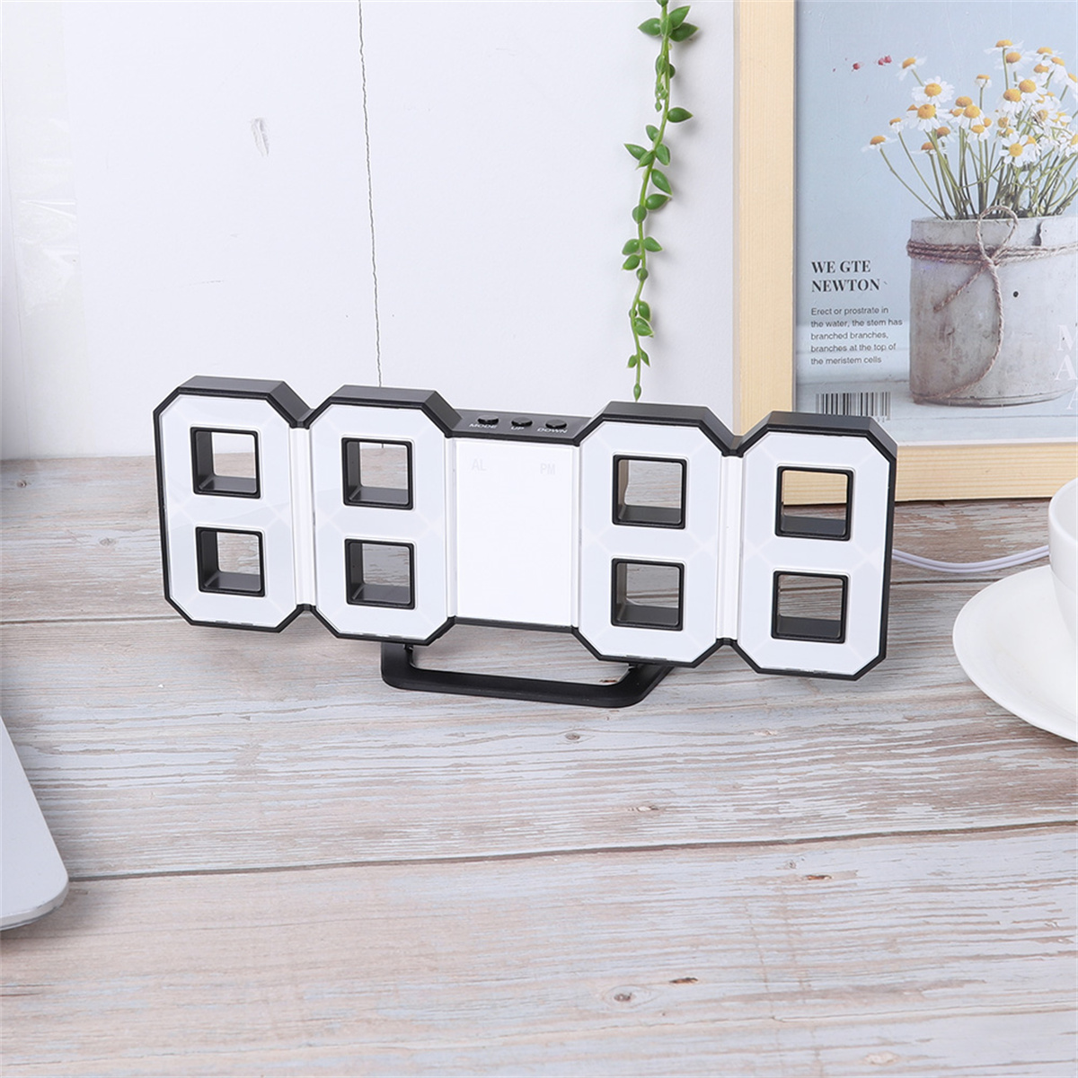Schwarze Digitaluhr mit weißen Zahlen auf einem Holztisch mit Rahmen.