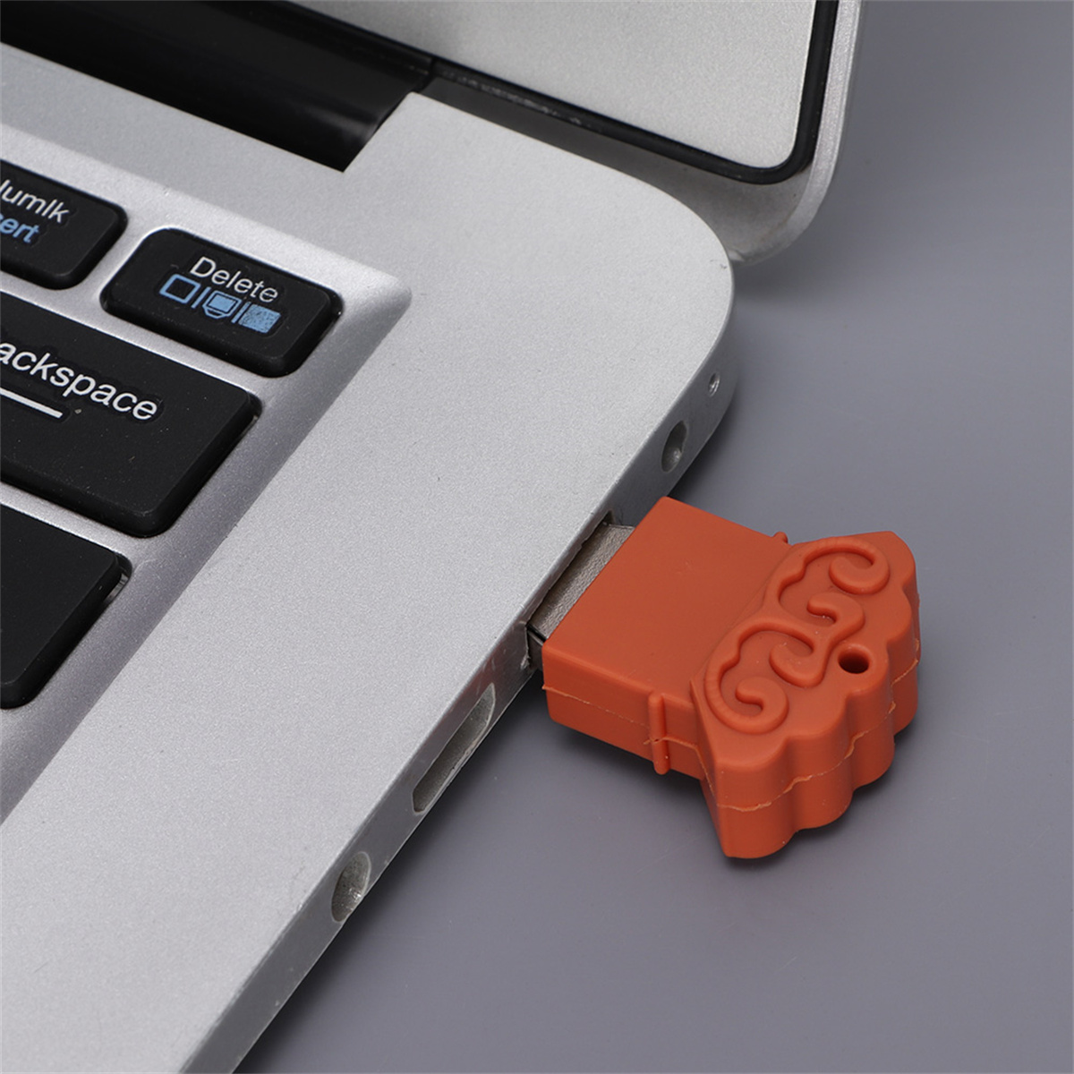 Ein silberner Laptop mit einem orangefarbenen USB-Stick. Der USB-Stick hat die Form einer Wolke.
