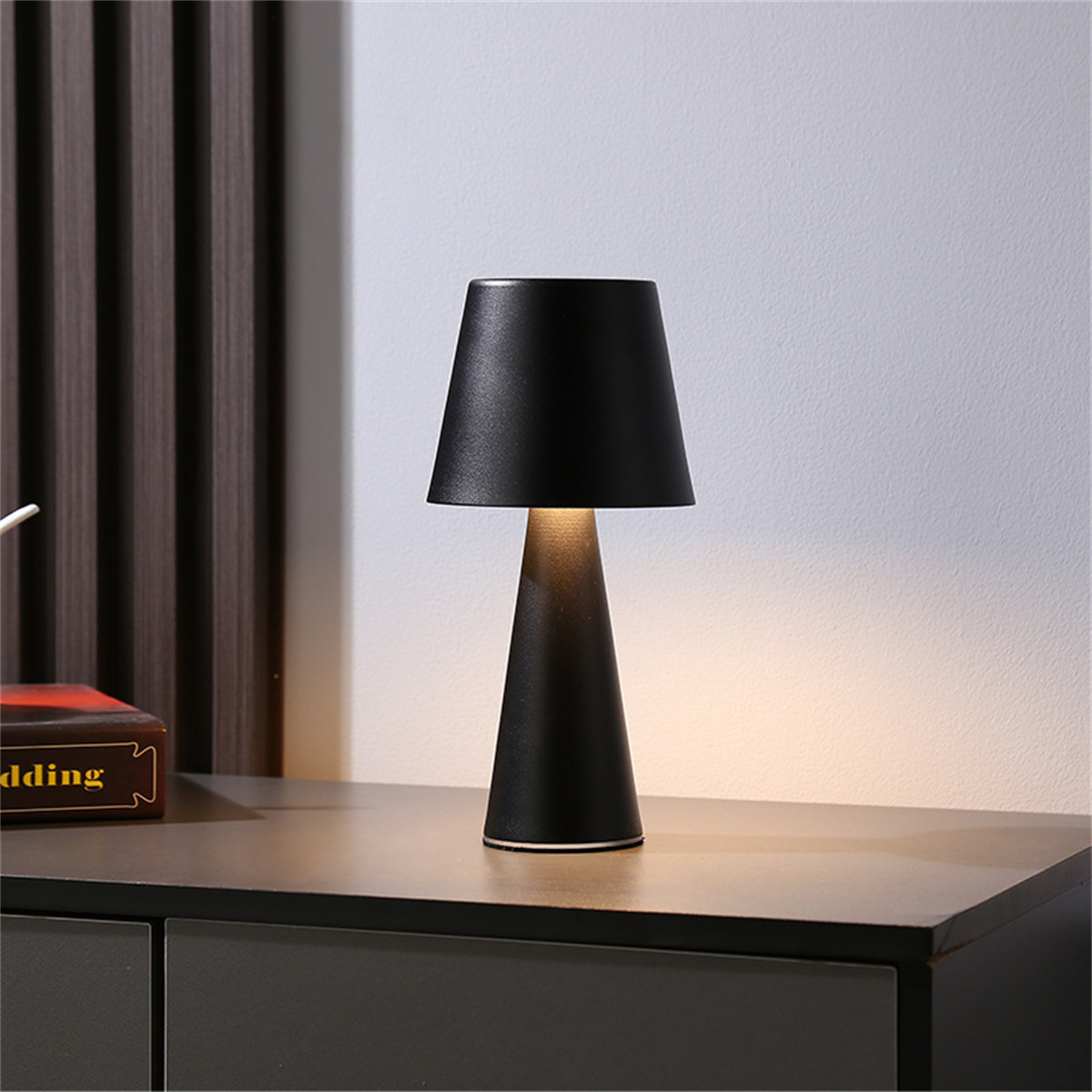 Schwarze Tischlampe mit konischem Fuß und Schirm. Sie steht auf einer grauen Oberfläche.