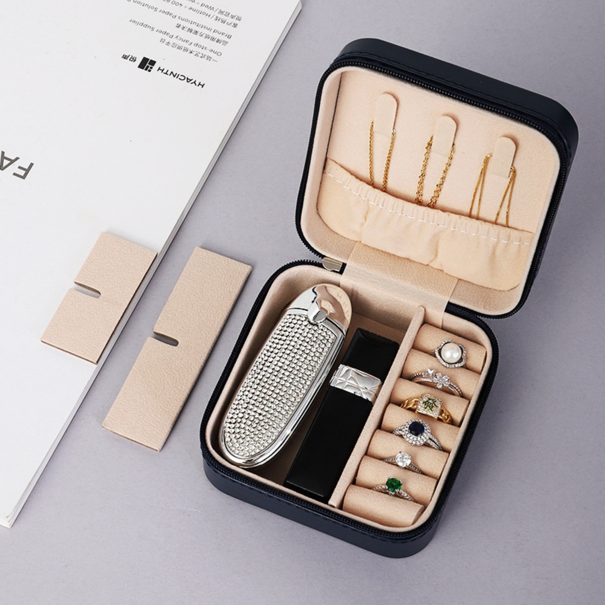 Geöffnete Schmuckschatulle mit Schmuck. Enthält Ringe, Halsketten und einen Lippenstift. Grauer Hintergrund.