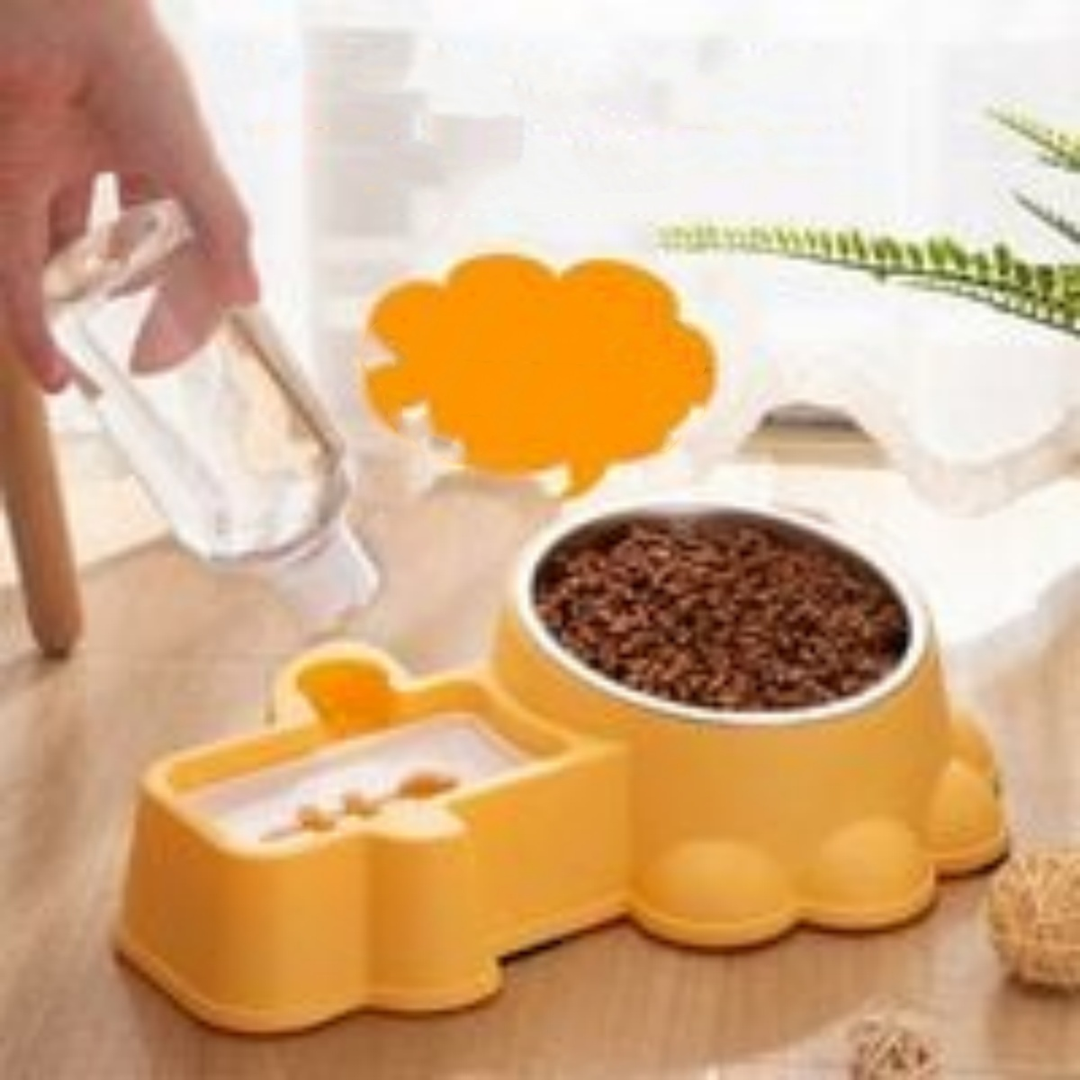 Eine gelbe Futterschüssel mit Futter. Eine Hand gießt Wasser in die Wasserschüssel. Der Hintergrund hat eine Pflanze.