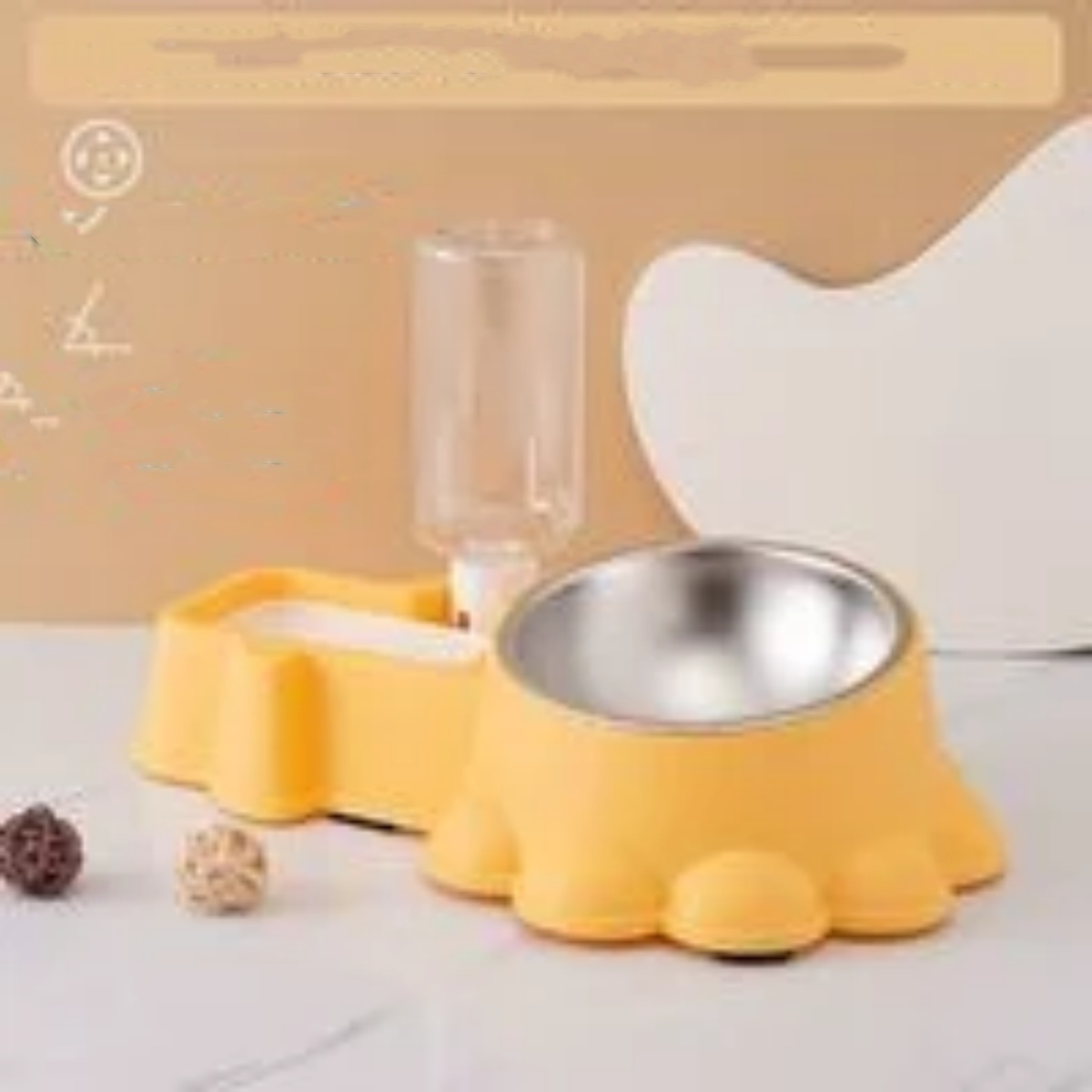 Gelbe Haustier-Schüssel mit zwei kleinen Bällen und einer Wasserflasche. Das Setup ist auf Beige.