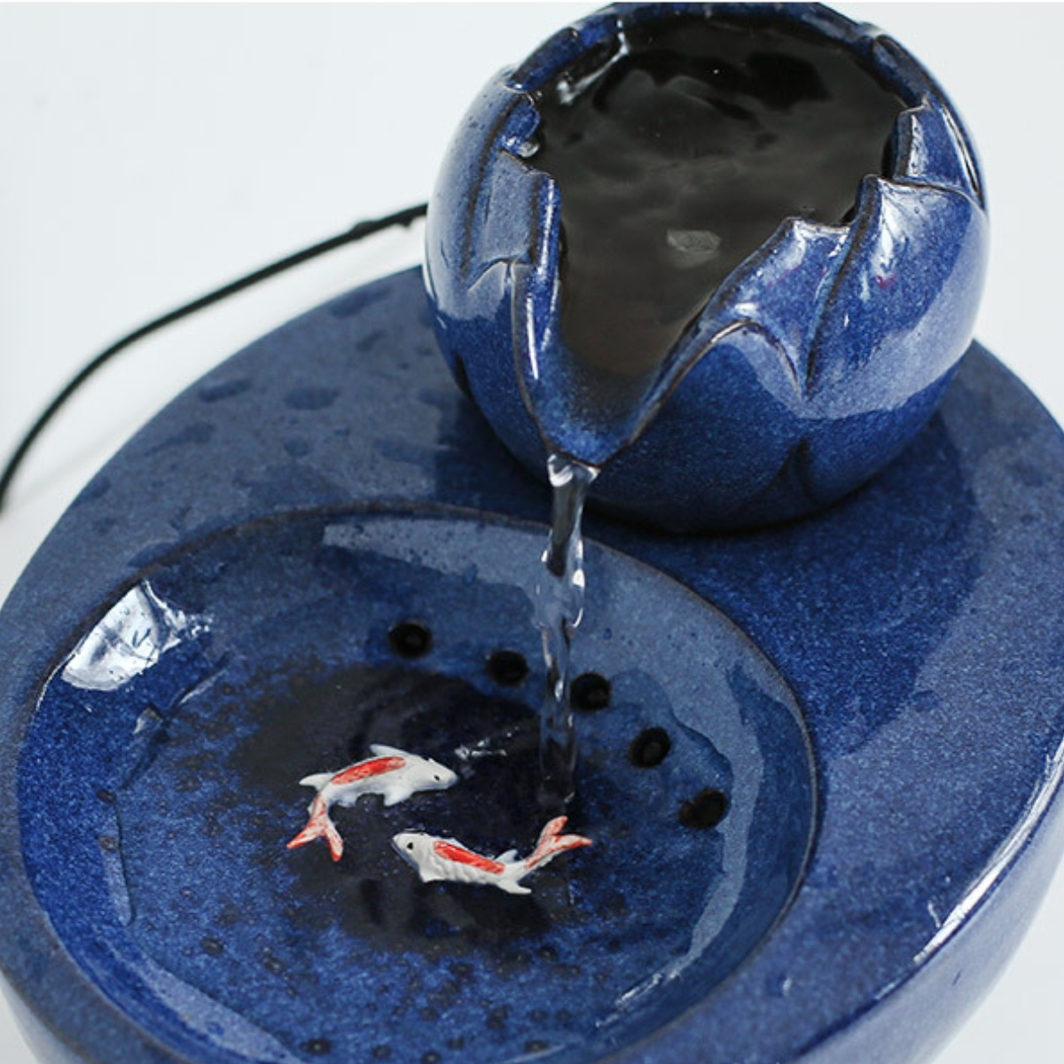 Ein blauer Keramikbrunnen mit fließendem Wasser. Zwei kleine Kois sind sichtbar.