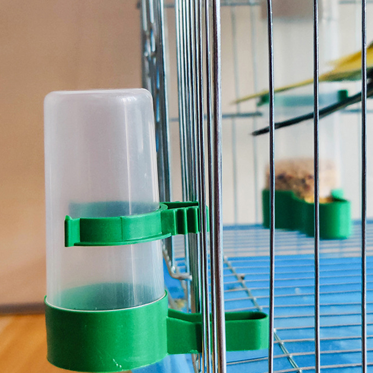 Grüner Vogelfutterspender in einem Käfig. Ein Vogel befindet sich im Käfig.