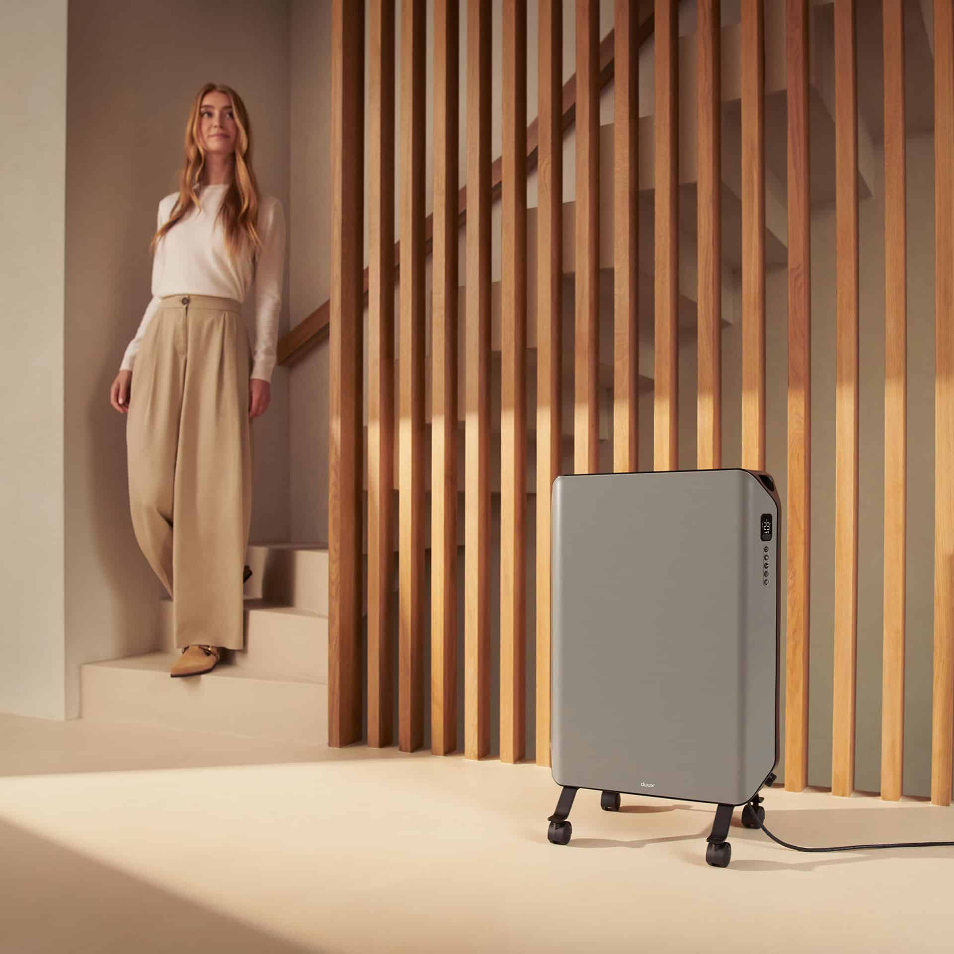 Frau geht eine Treppe hinunter, vorbei an einer grauen Elektroheizung auf einem Ständer. Holzlattensichtschutz im Hintergrund.