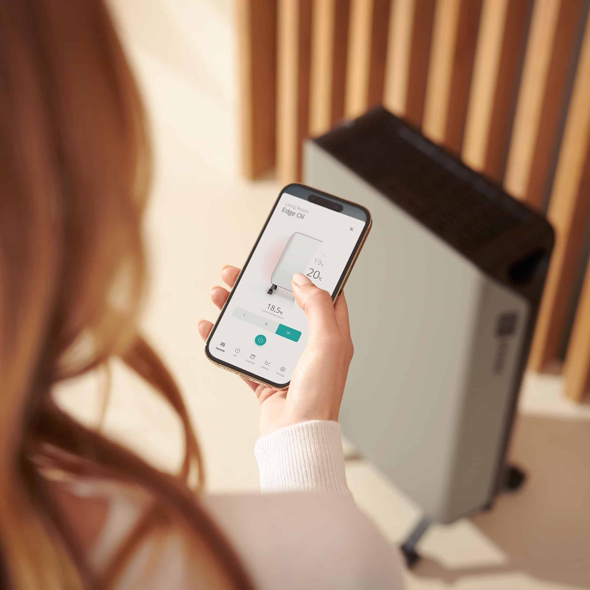 Frau hält Telefon mit App, im Hintergrund ein smarter Heizkörper.