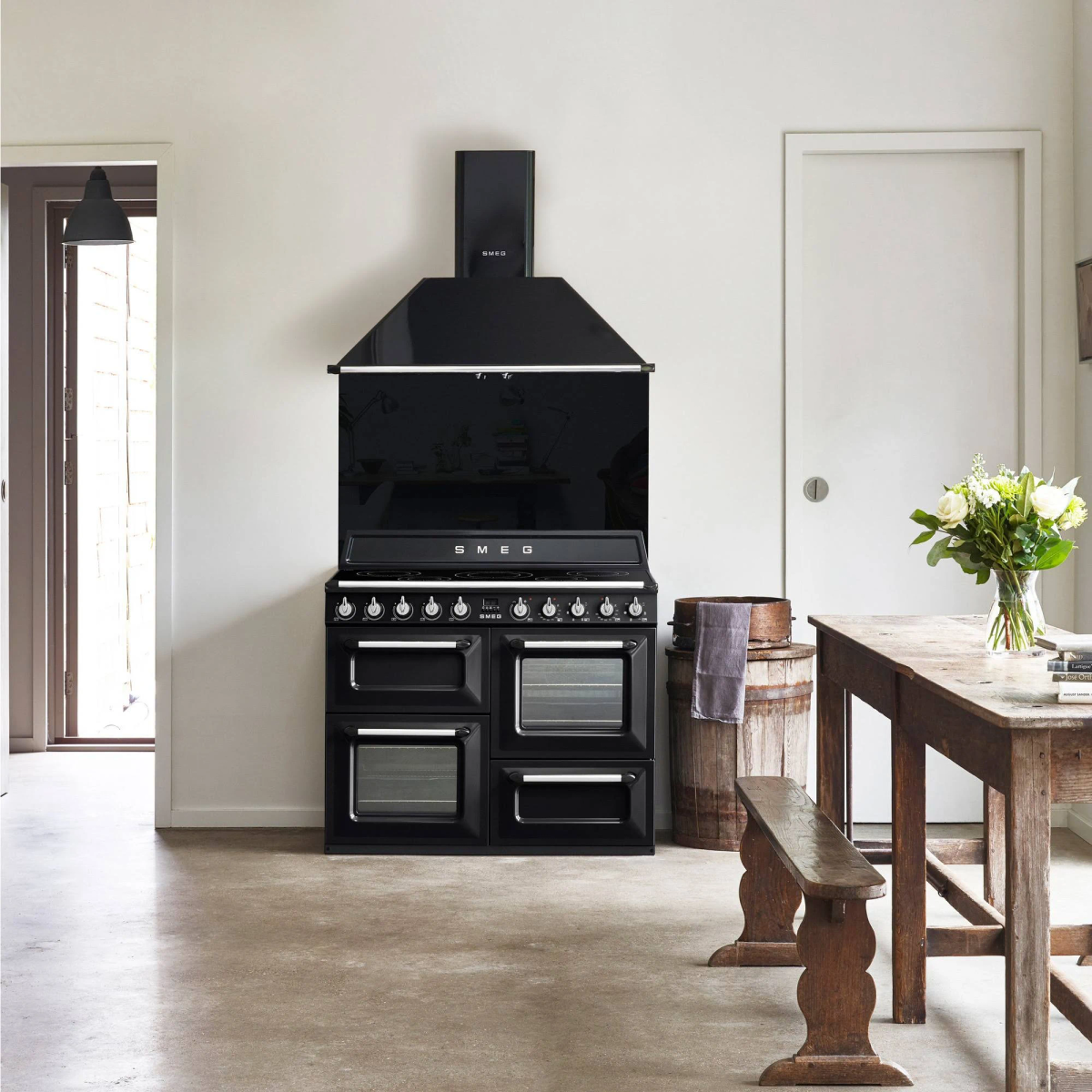 Cocina SMEG negra en una cocina. Incluye campana extractora, horno y mesa.