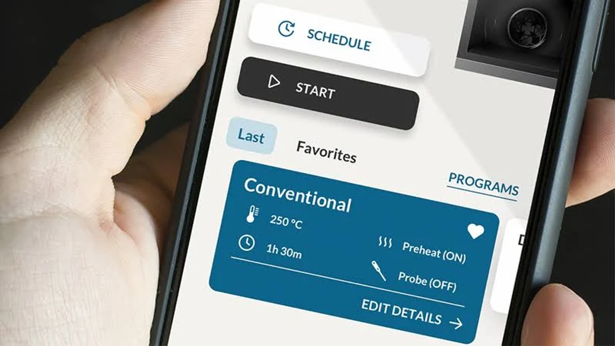 Una mano che tiene uno smartphone con un'app di cucina aperta. Mostra le impostazioni del forno. Lo sfondo è sfocato.