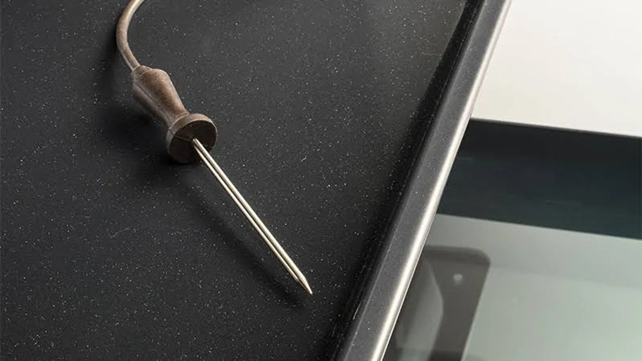 Una sonda alimentare metallica su una superficie nera, con la punta rivolta verso il basso.